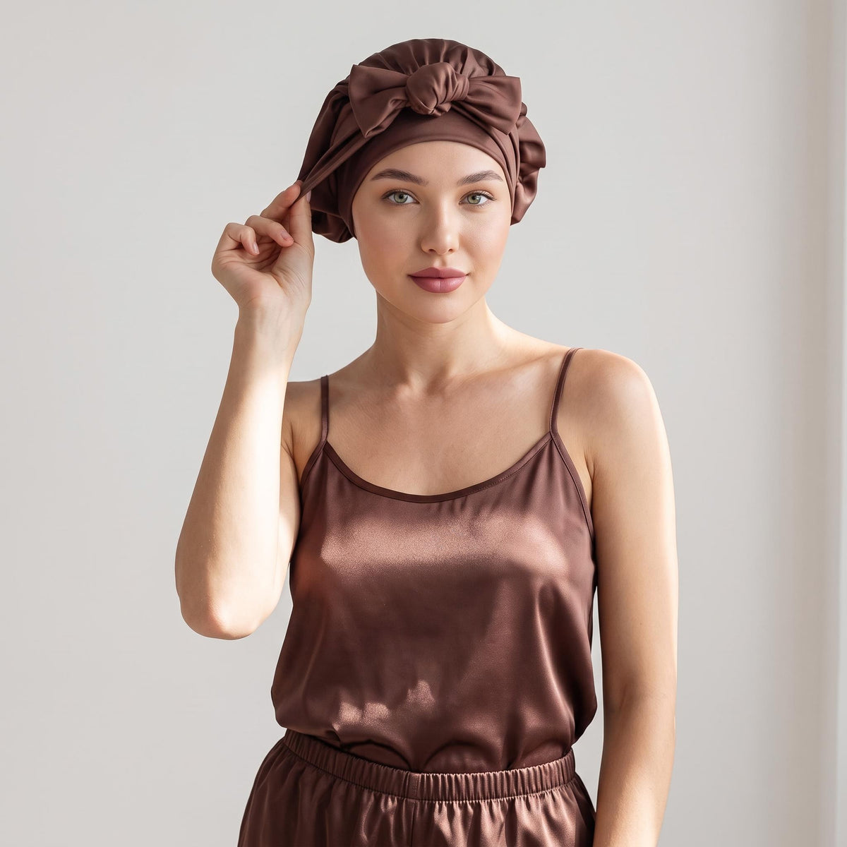 Woman wearing a brown mulberry silk sleep bonnet with an elegant front bowknot tie, styled with matching satin pajamas.