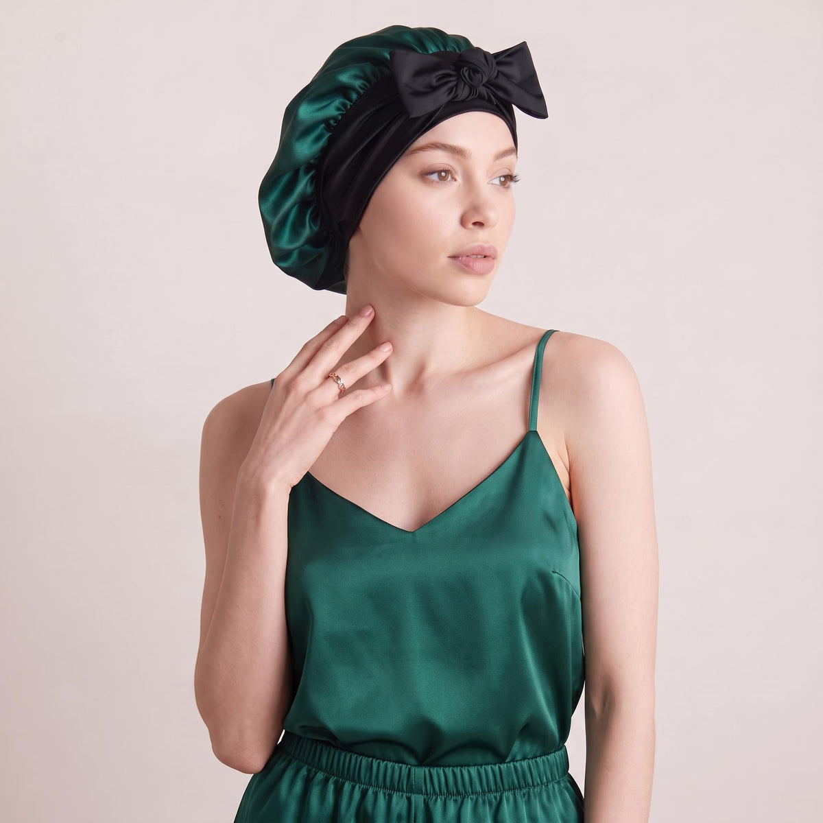 Emerald green mulberry silk sleep bonnet with a black bow tie worn by a woman in a matching satin camisole.