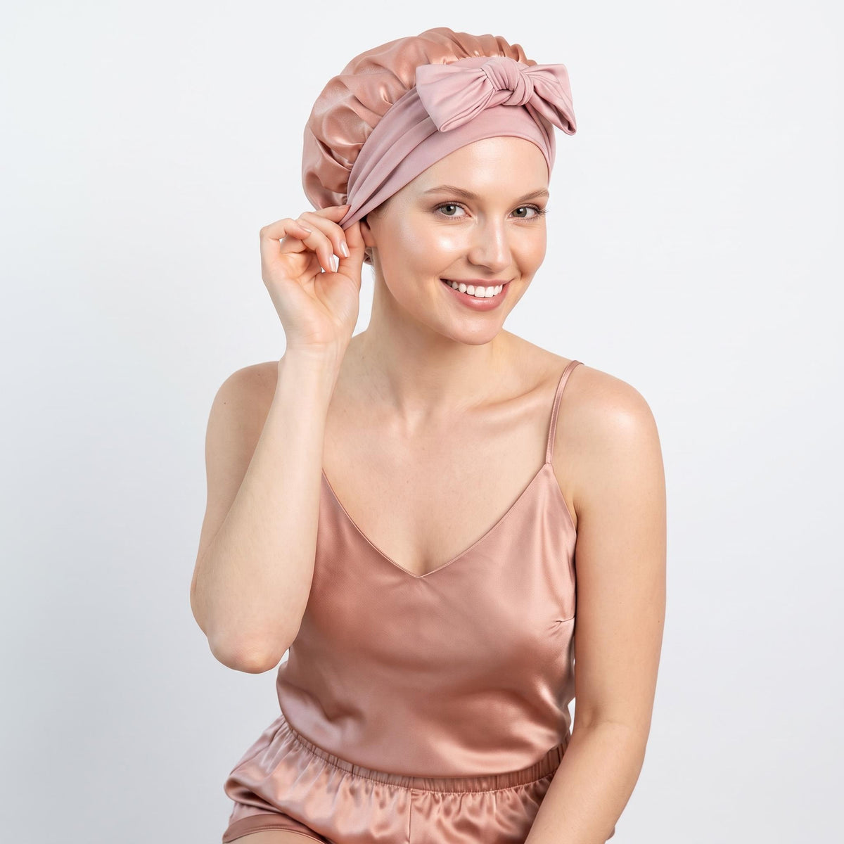 Woman wearing a dusty pink mulberry silk sleep bonnet with an elegant front bow tie against a white background.