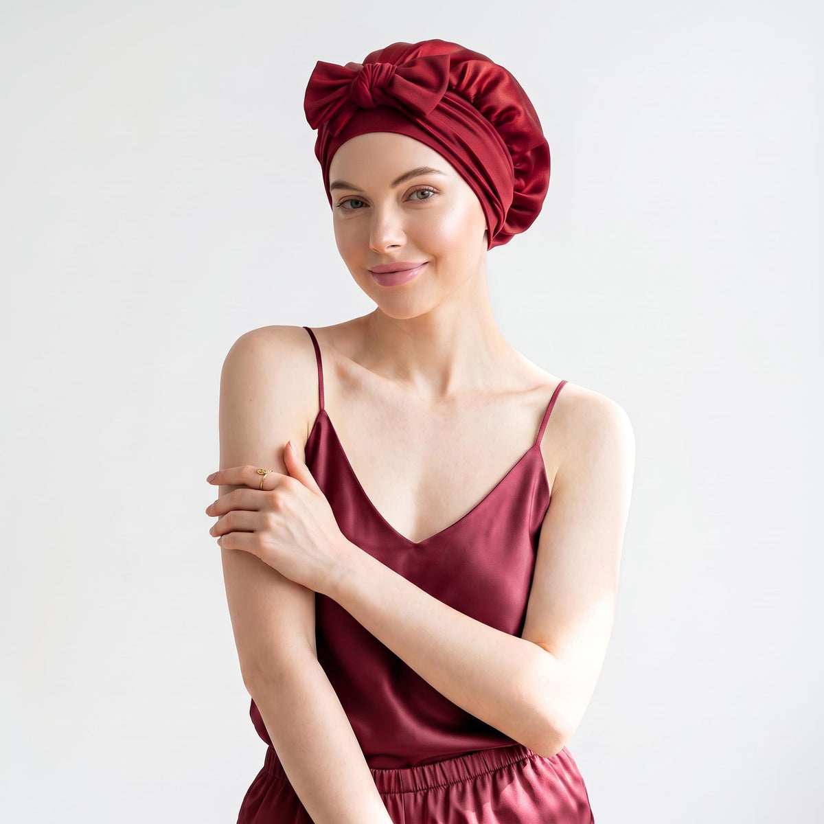 Woman wearing a deep red mulberry silk sleep bonnet with a stylish front bow tie, matching her satin camisole.