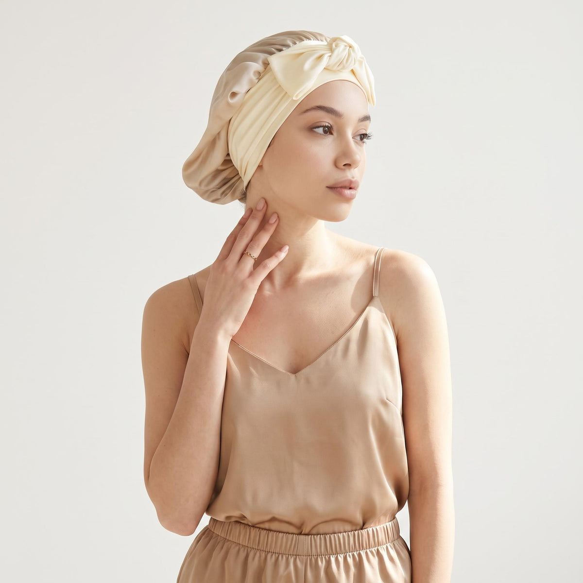 Champagne-colored mulberry silk sleep bonnet with an adjustable bowknot tie worn by a woman in a matching silk camisole.