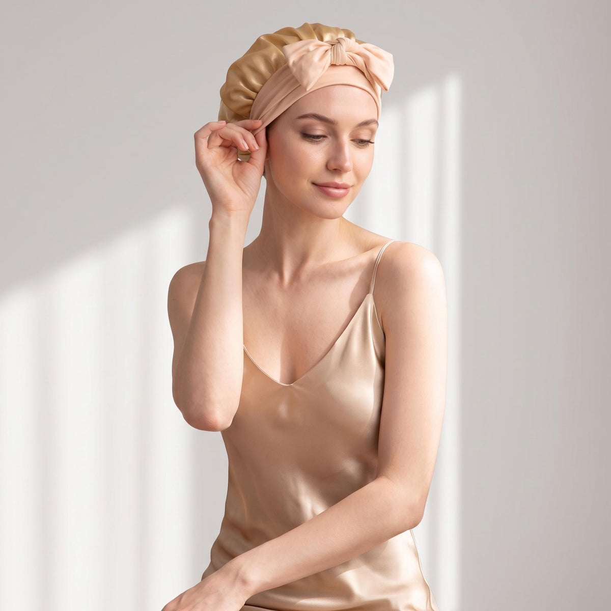 Woman wearing a champagne-colored 100% mulberry silk sleep bonnet with an adjustable bow tie for hair protection.