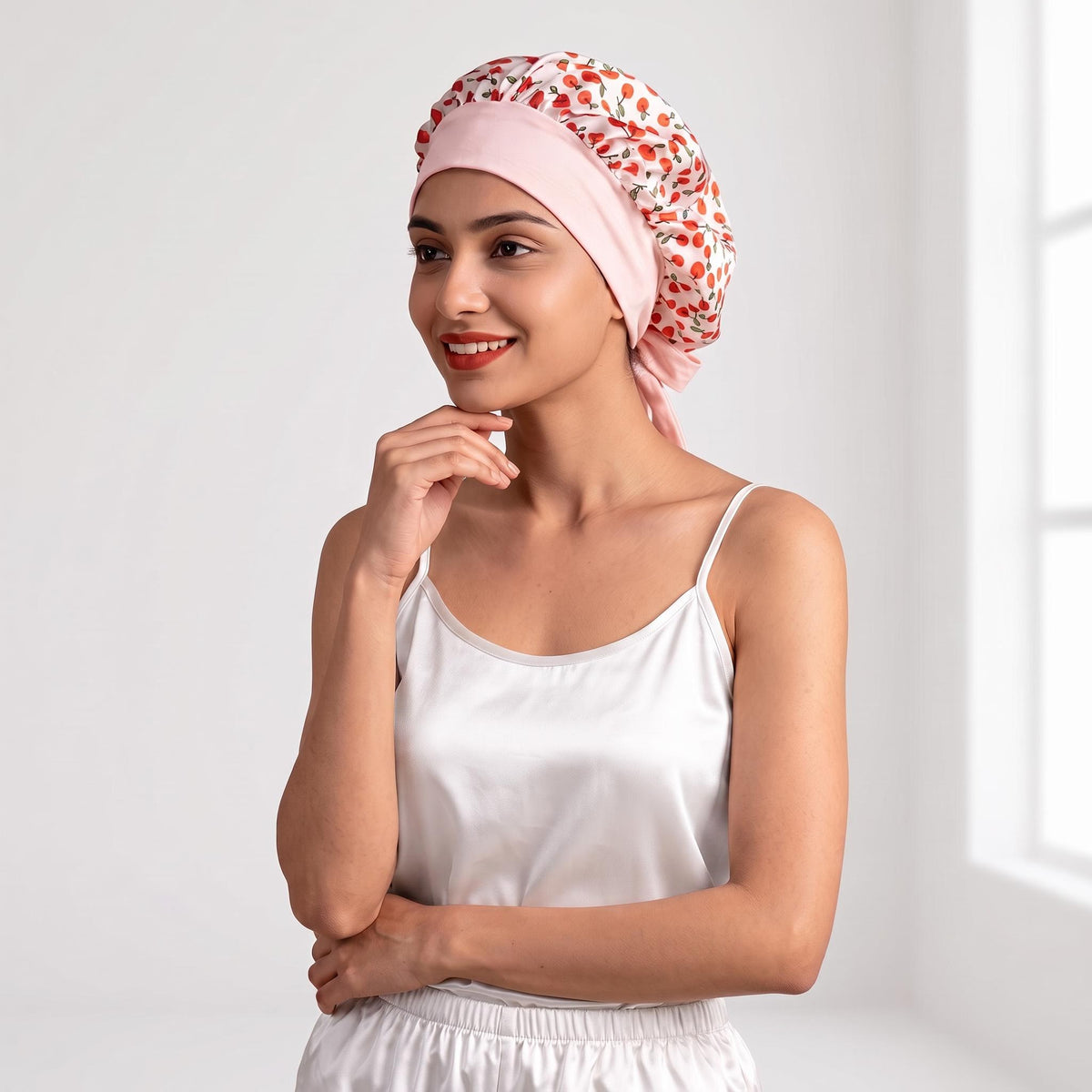 Woman wearing a mulberry silk sleep bonnet with a pink cherry print and adjustable bow tie for hair protection.