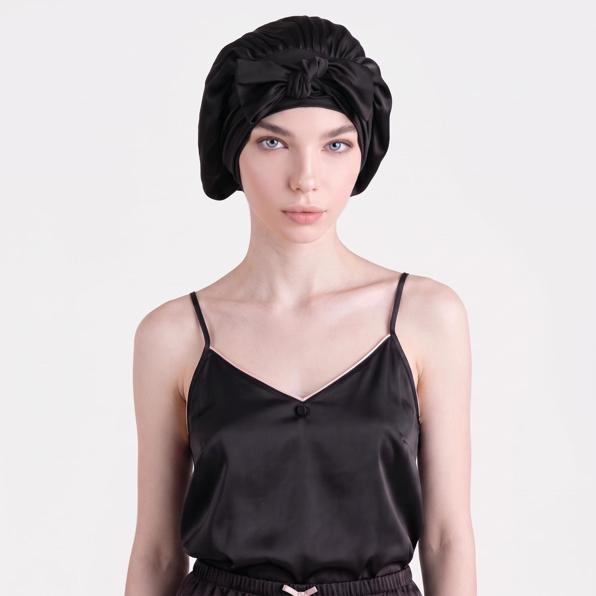 Model wearing a black 100% mulberry silk sleep bonnet with an elegant front bow tie design against a white background.