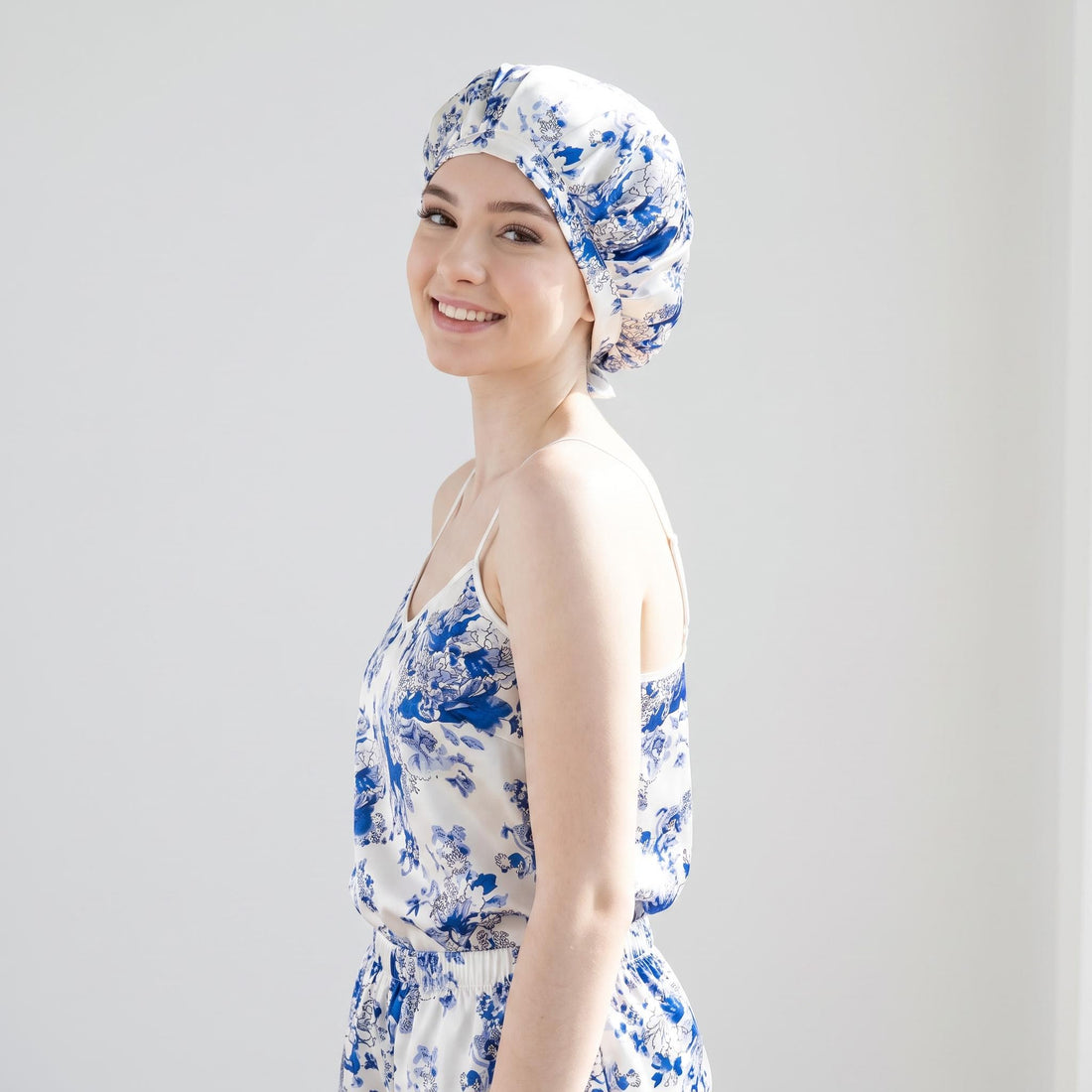Woman wearing a blue and white floral mulberry silk sleep bonnet with adjustable ties for hair protection.