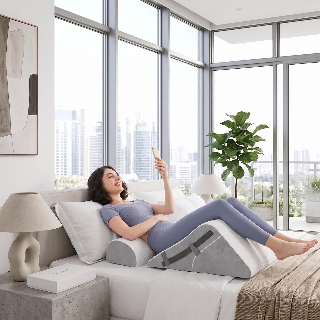 Woman sitting in bed using a grey, 3-piece adjustable memory foam wedge pillow set for ergonomic back and neck support.