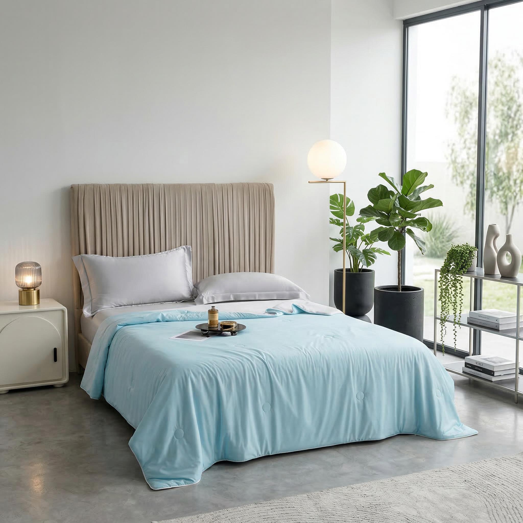 Light blue cooling blanket on a bed with a beige headboard in a modern bedroom.