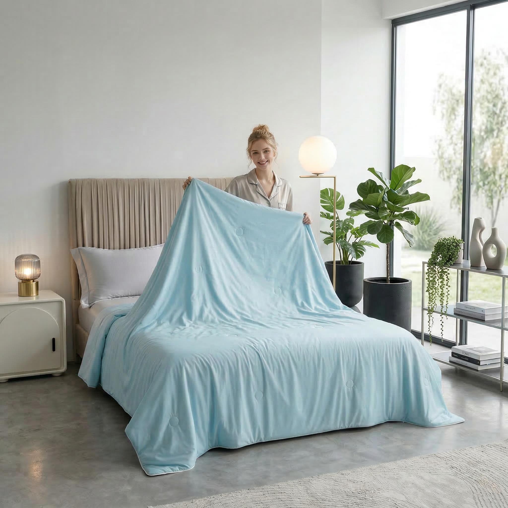 Smiling woman in pajamas making a bed with a light blue cooling blanket, showcasing its soft texture.