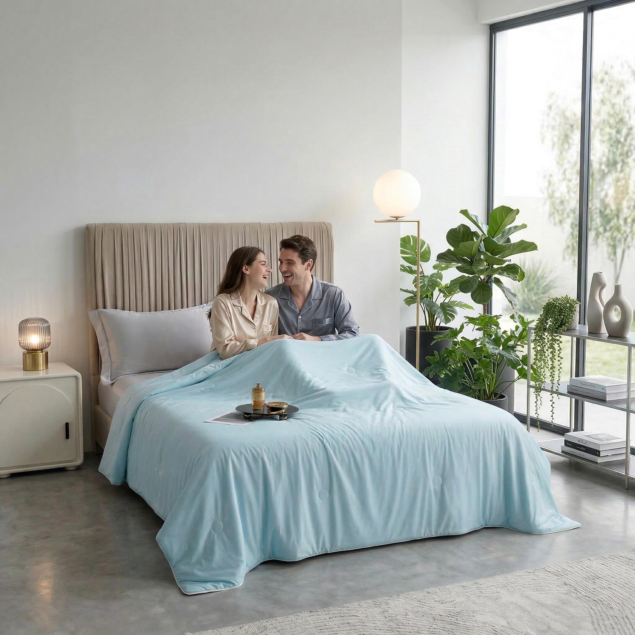 Couple smiling in bed under a light blue AC cooling blanket, with a breakfast tray.