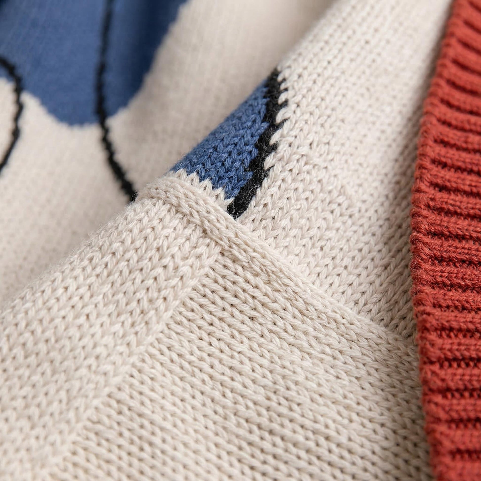 Close-up of an abstract knitted throw blanket in earthy tones with blue organic shapes.