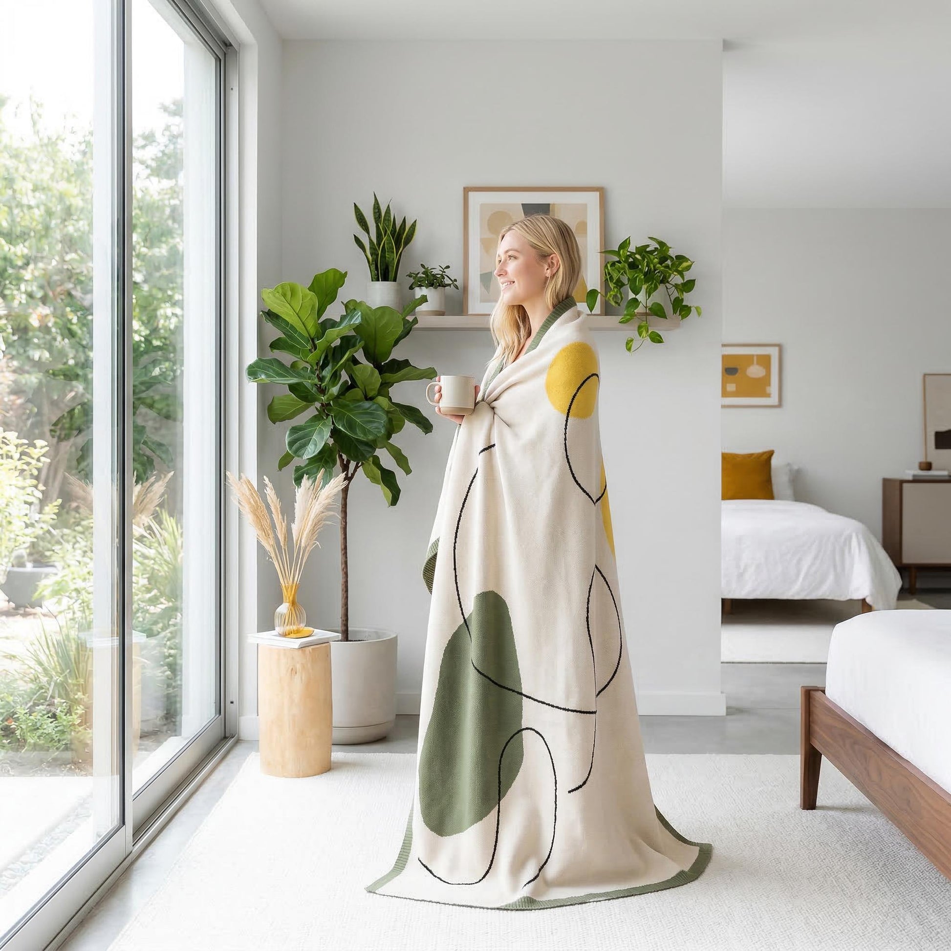 Woman wrapped in an Abstract Knitted Throw Blanket with earthy tones and organic shapes, holding a mug.