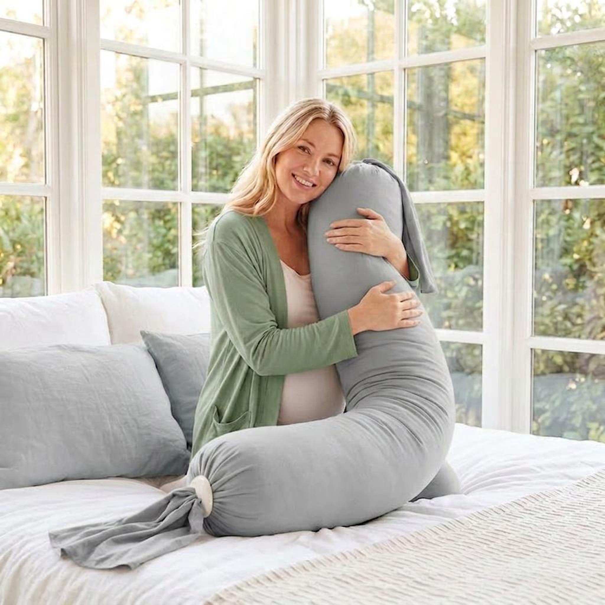 Smiling pregnant woman hugging a light gray adjustable U-shaped body pillow with a stretch-knit cover.