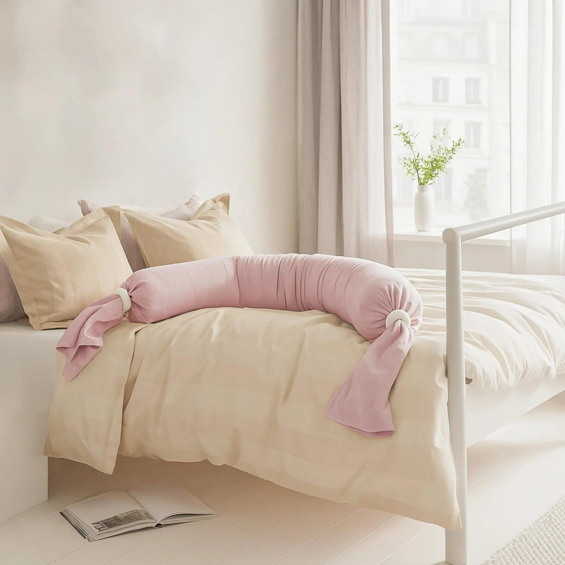 Pink adjustable U-shaped pregnancy body pillow on a bed with beige bedding.