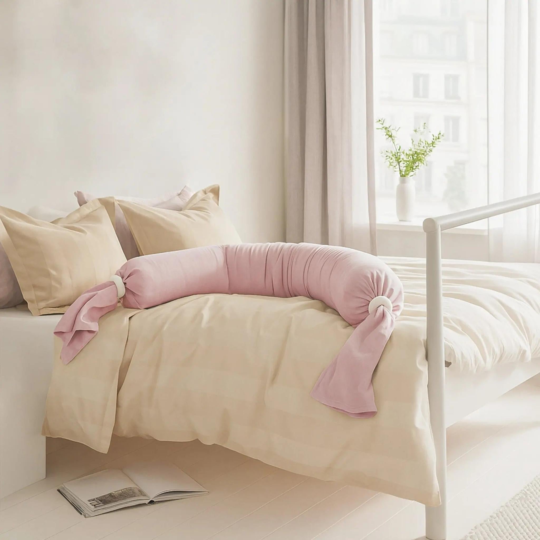Pink adjustable U-shaped pregnancy body pillow on a bed with beige bedding.