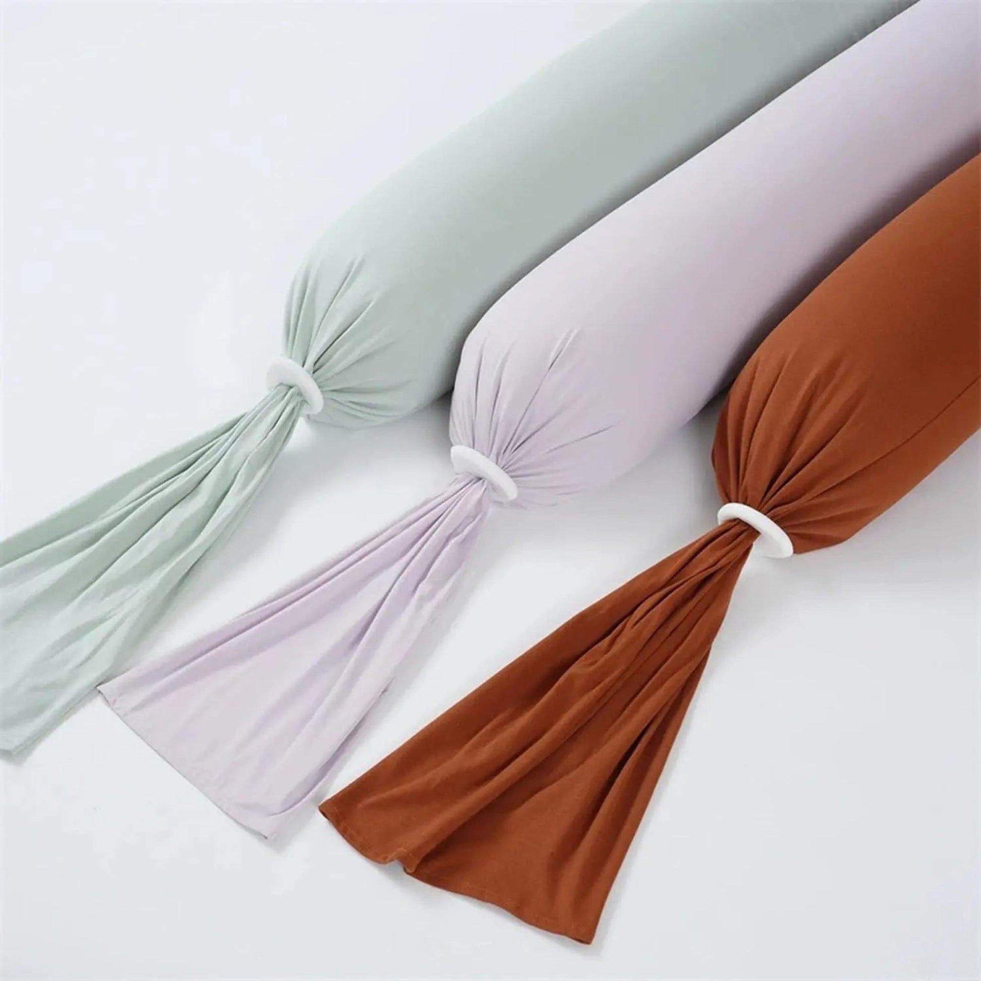 Three adjustable U-shaped pregnancy body pillows in sage green, lavender, and terracotta with white rings.