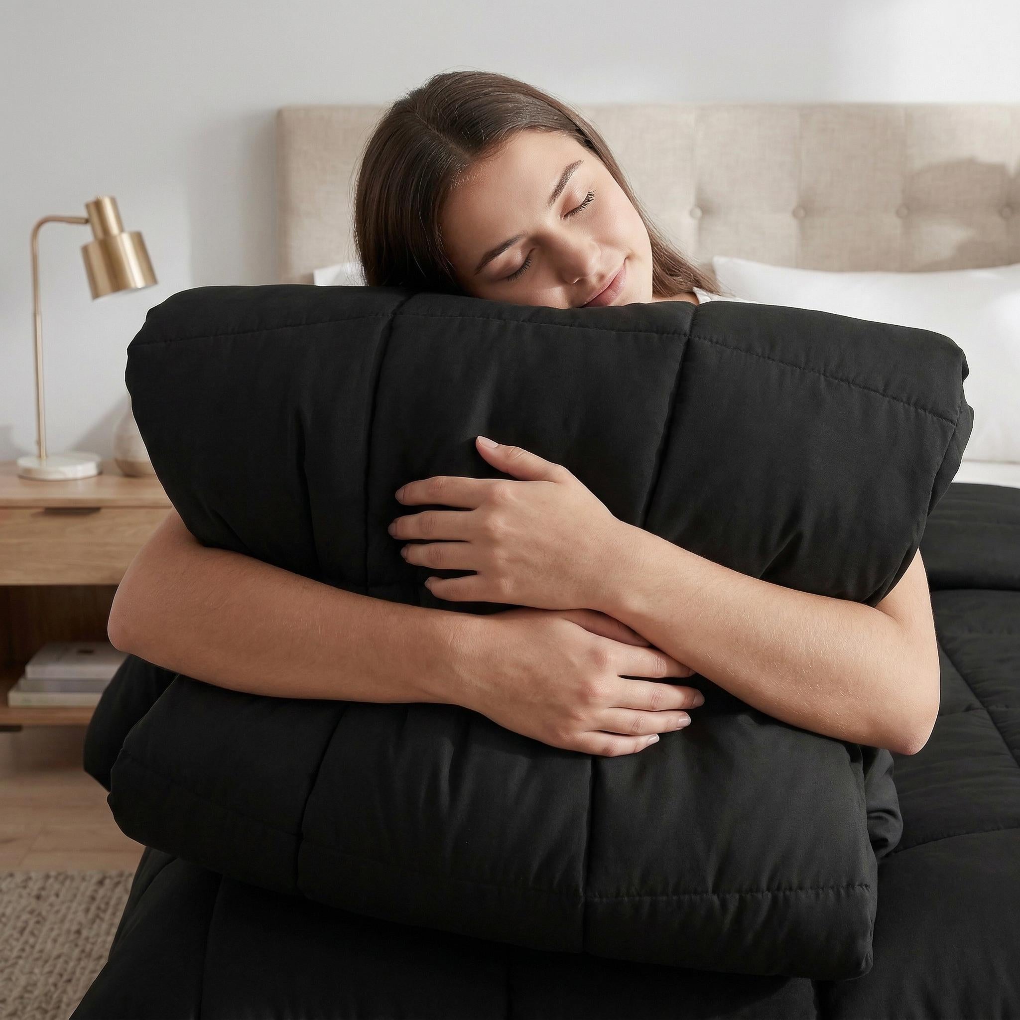 Woman hugging a soft black microfiber all-season comforter with box stitching in a bedroom.