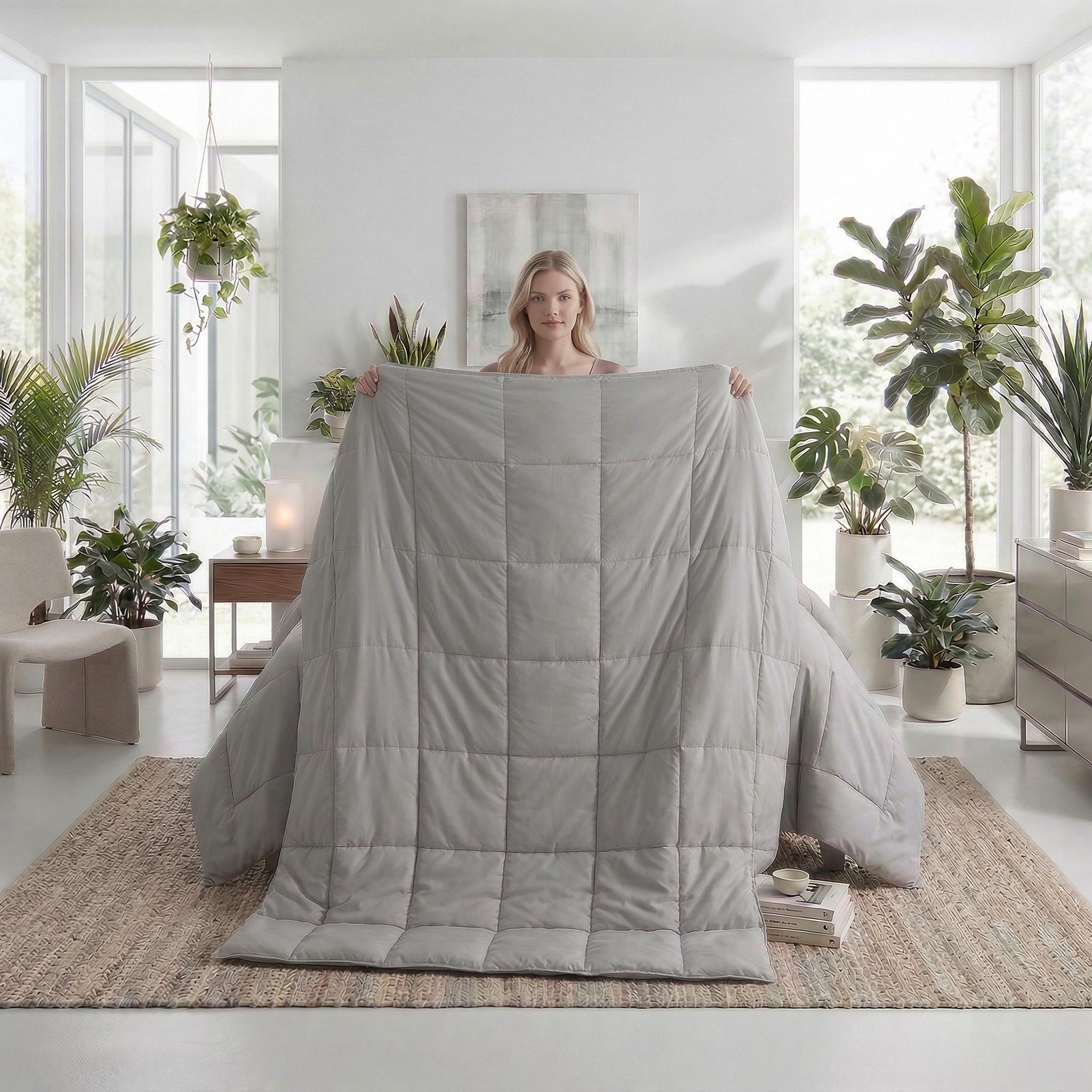 Blonde woman holding a light gray microfiber all-season comforter with box stitching.