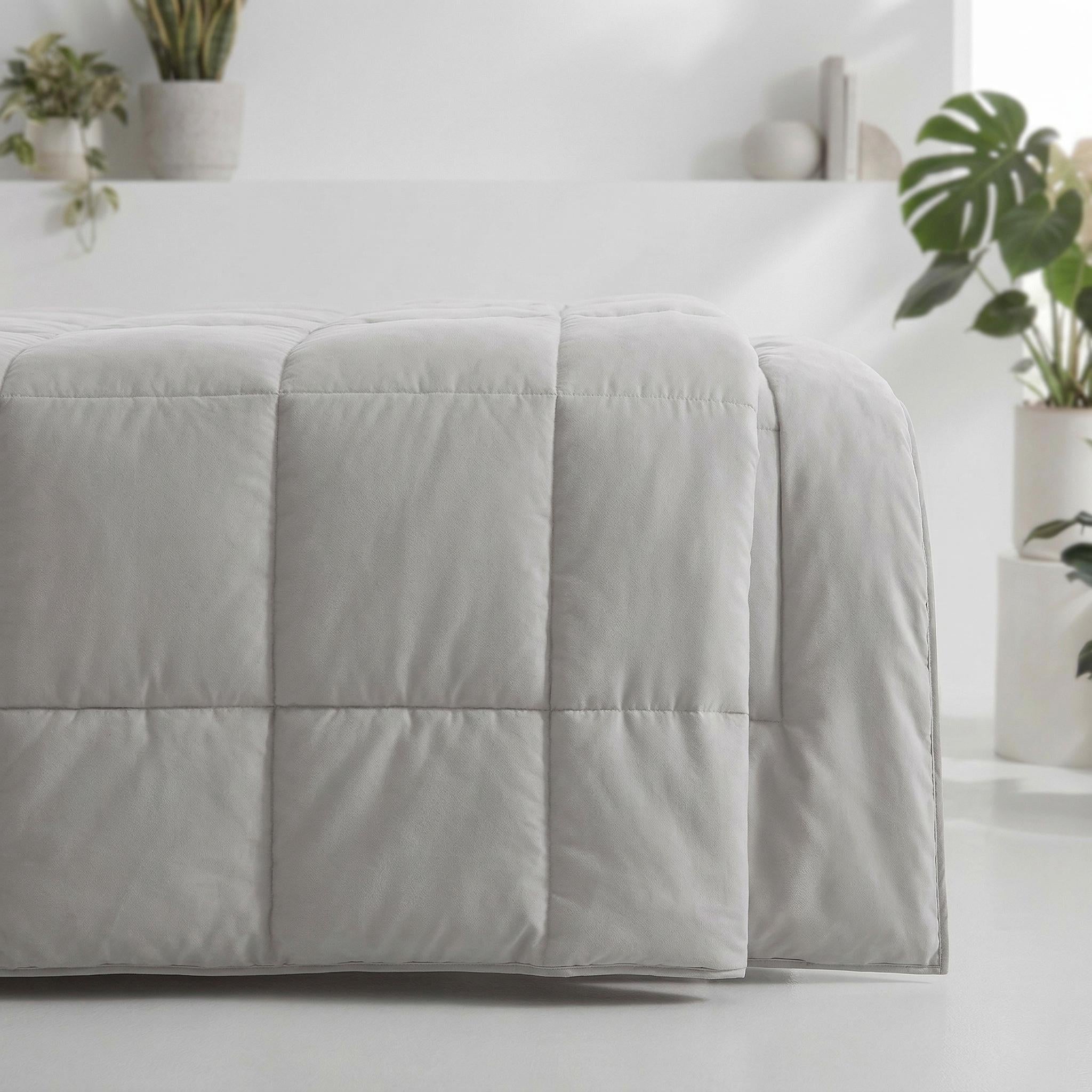 Light gray microfiber all-season comforter with box stitching, draped over a bed.