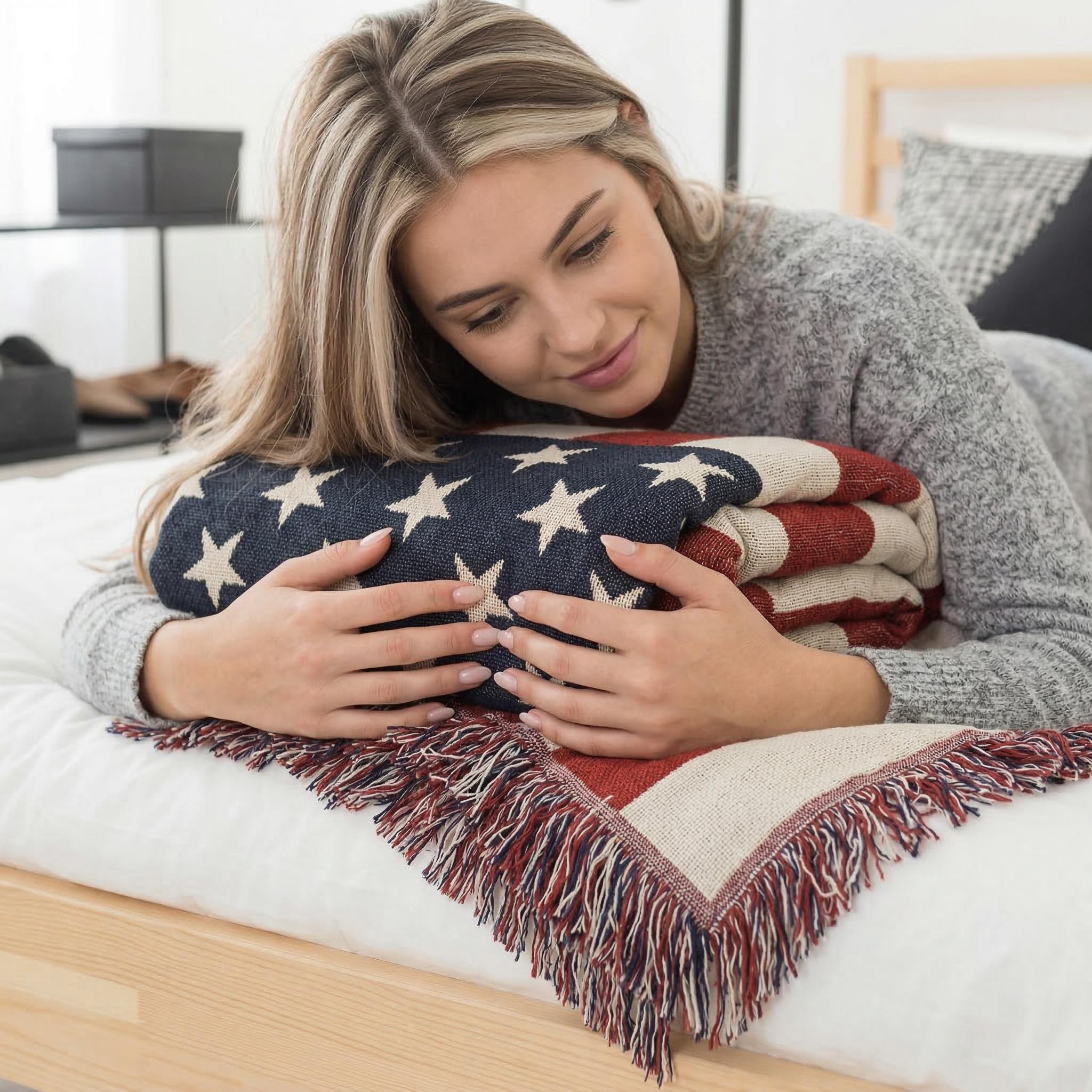 Woman on bed holding a folded American flag knitted throw blanket with fringe.