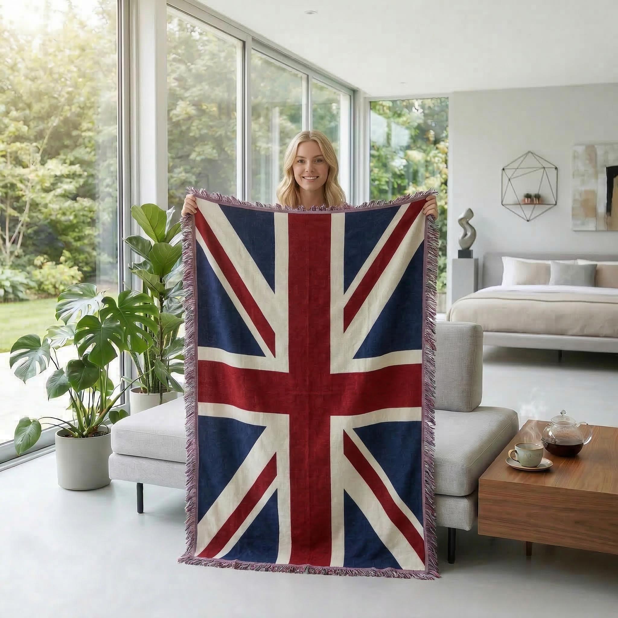 Blonde woman holding a knitted throw blanket featuring a Union Jack flag design in a modern living room.