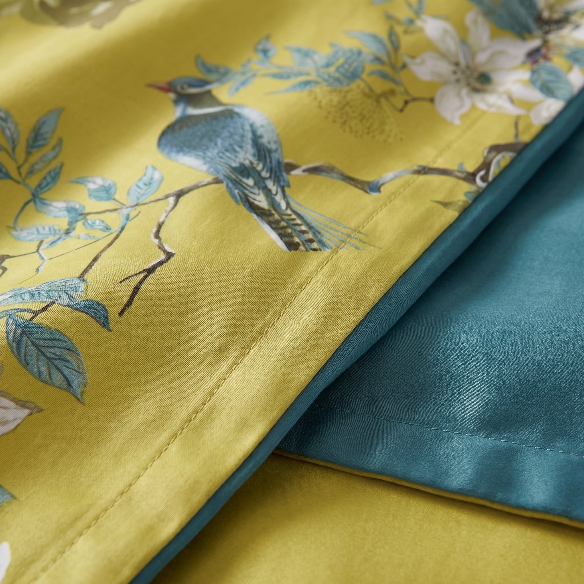 Aurelia Aviary cotton sateen bedding with golden ground, blue bird, floral design, and deep teal reverse.