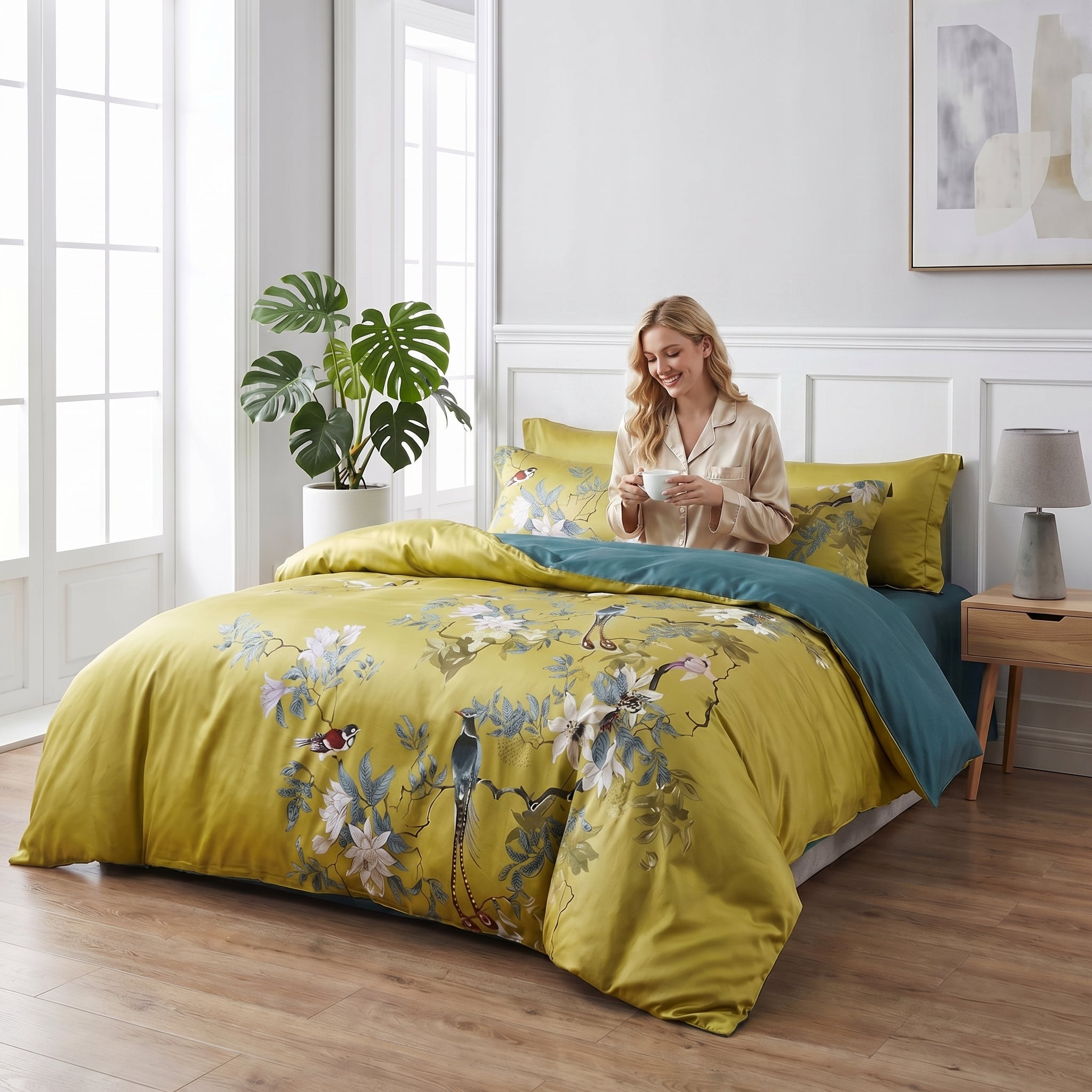 Aurelia Aviary cotton bedding set with golden floral bird design and deep teal reverse, on a bed with a smiling woman.