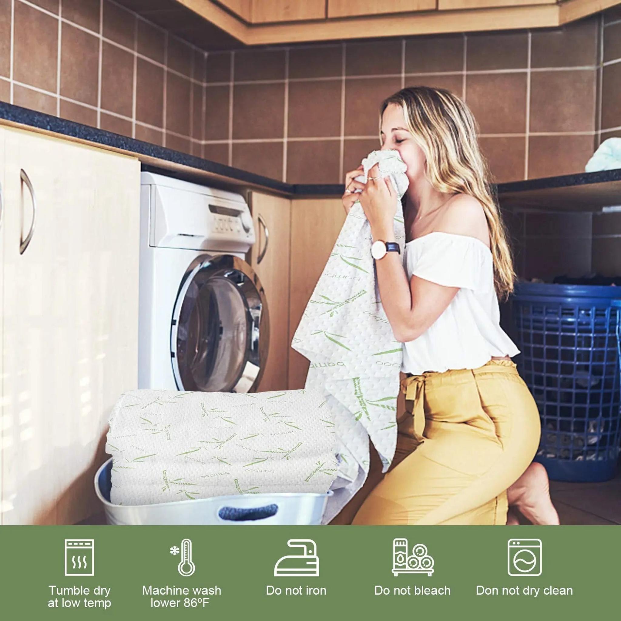 Woman kneeling in a laundry room, smelling a soft, white bamboo fiber mattress protector with green bamboo leaf patterns.