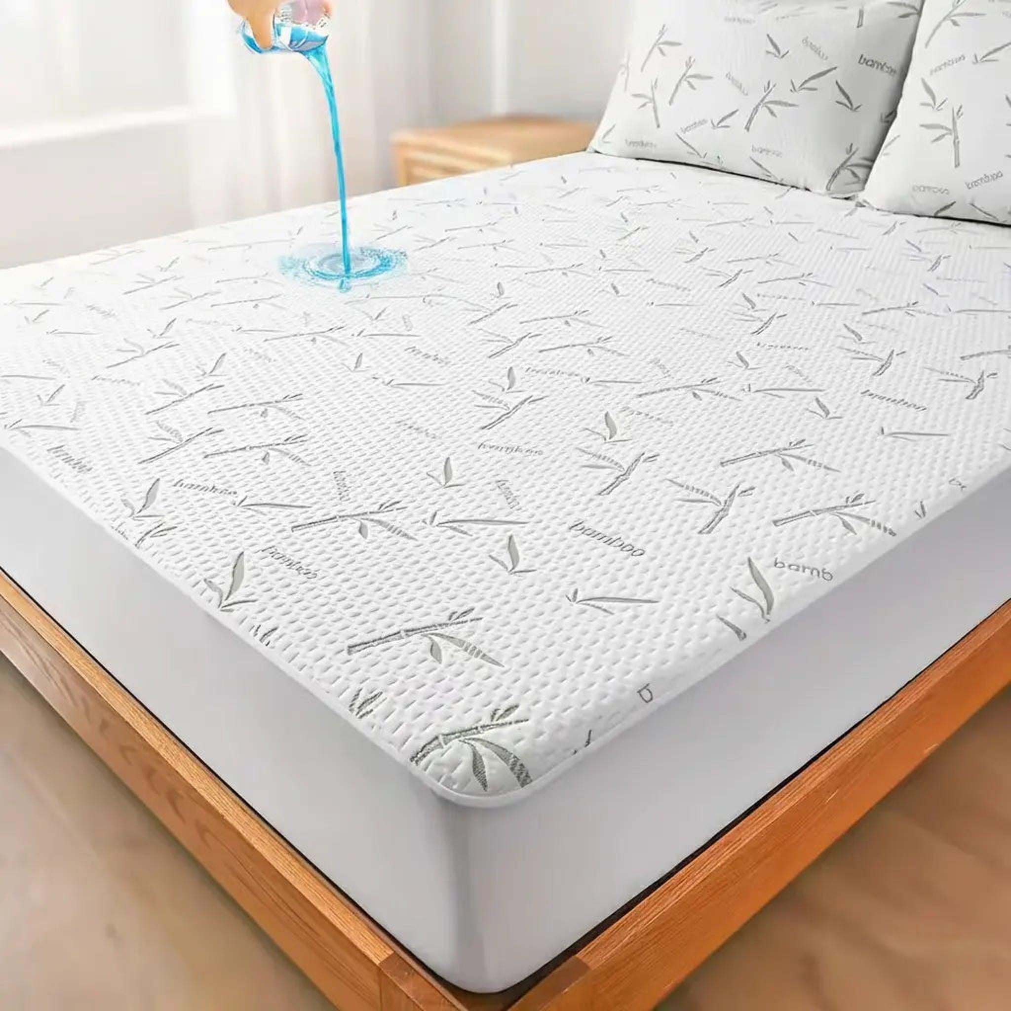 White bamboo fiber mattress protector with gray bamboo leaf pattern, showing blue liquid beading on its waterproof surface.