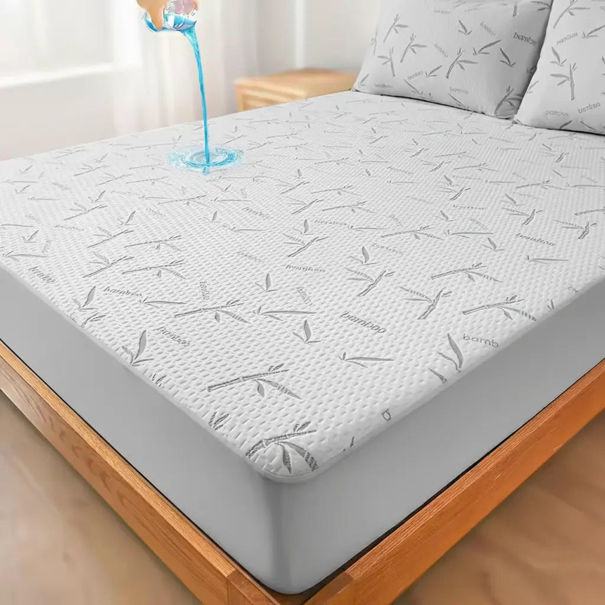 White bamboo fiber mattress protector with grey bamboo leaf pattern, shown on a bed with water pouring on it.