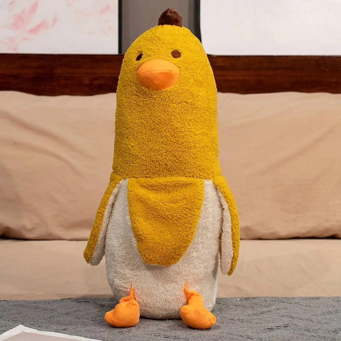 Woman hugging a large yellow banana duck plush pillow on a bed, with a smaller one beside her.