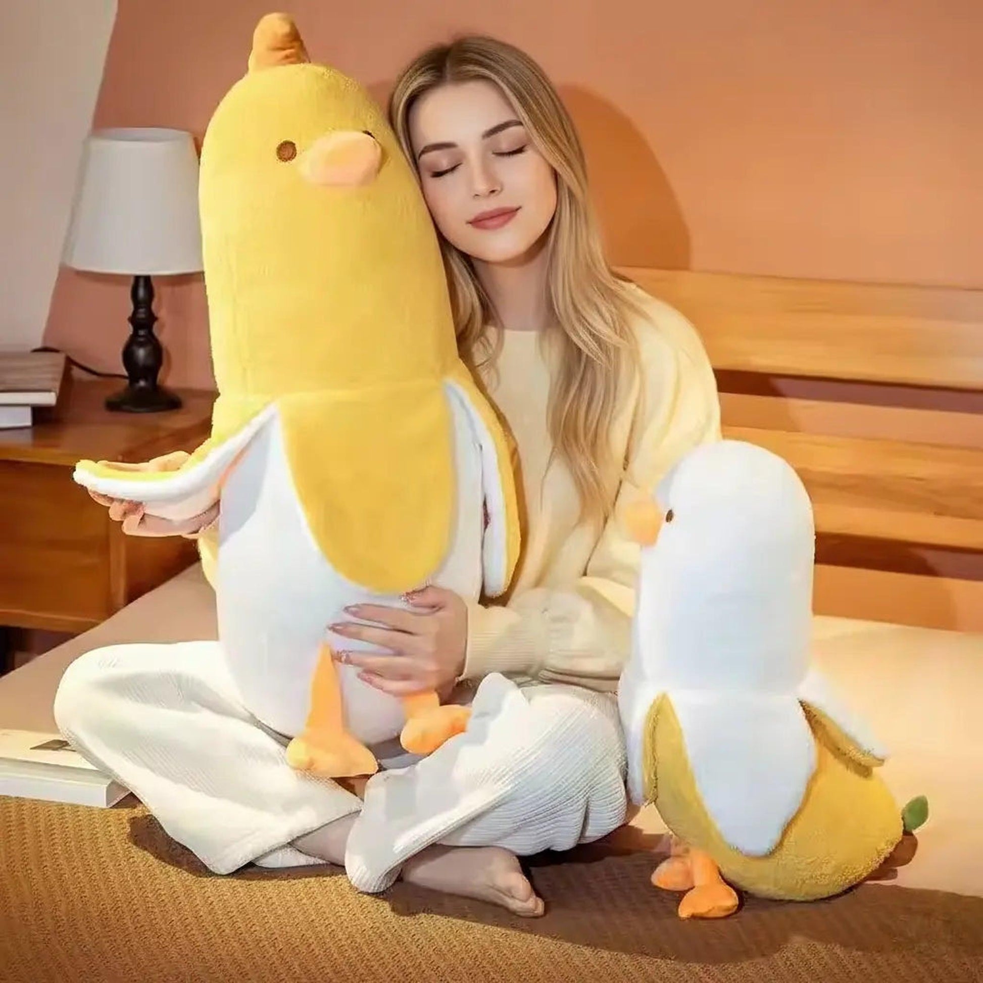 Blonde woman hugging a large yellow banana duck plush pillow, with a smaller one beside her.