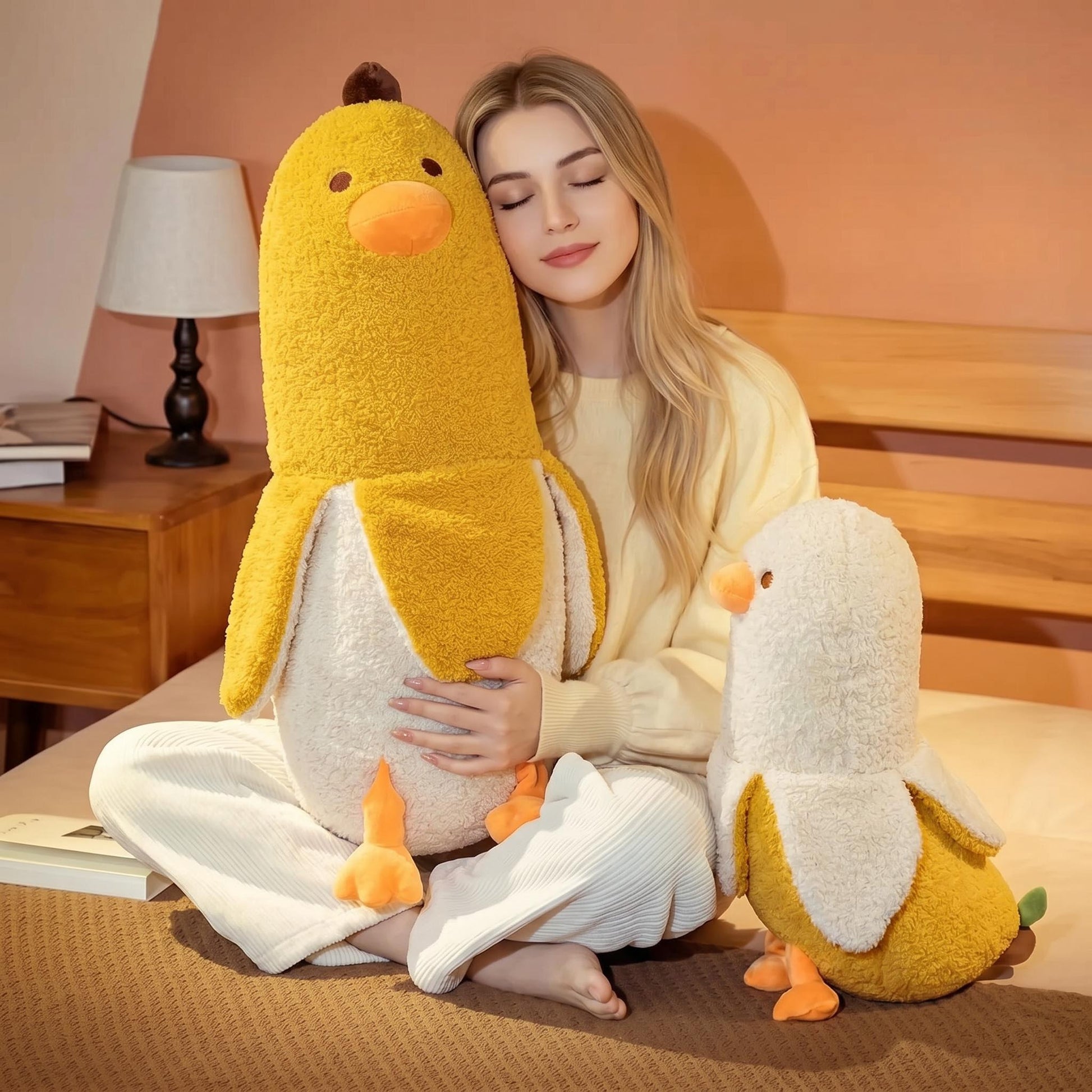 Blonde woman hugging a large yellow banana duck plush pillow, with a smaller one beside her.