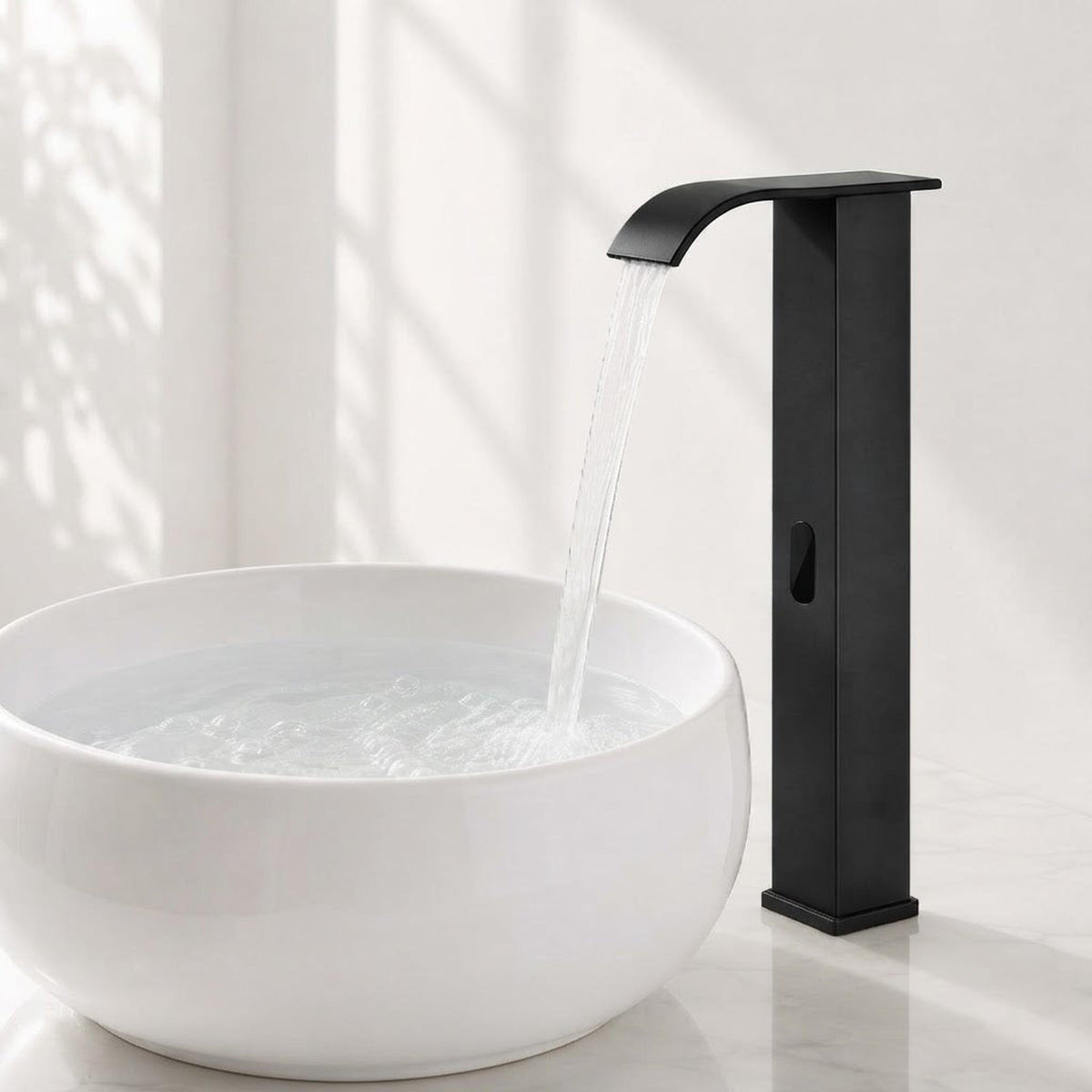 Modern matte black touchless bathroom faucet with a waterfall spout, pouring water into a white ceramic basin.