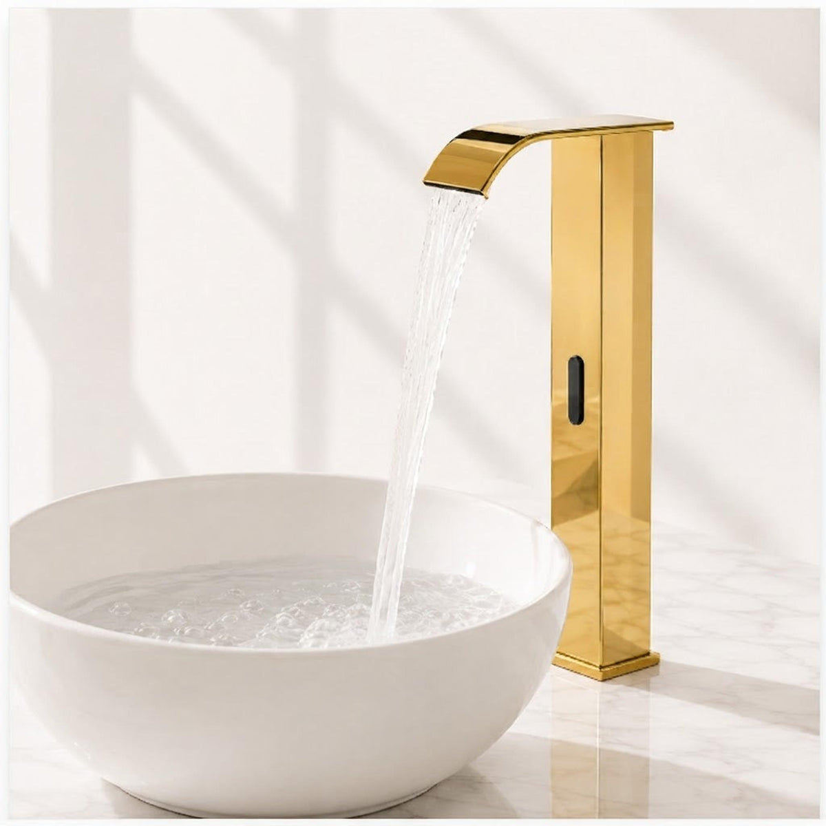 Modern gold touchless bathroom faucet with a waterfall spout and automatic sensor over a white ceramic basin.