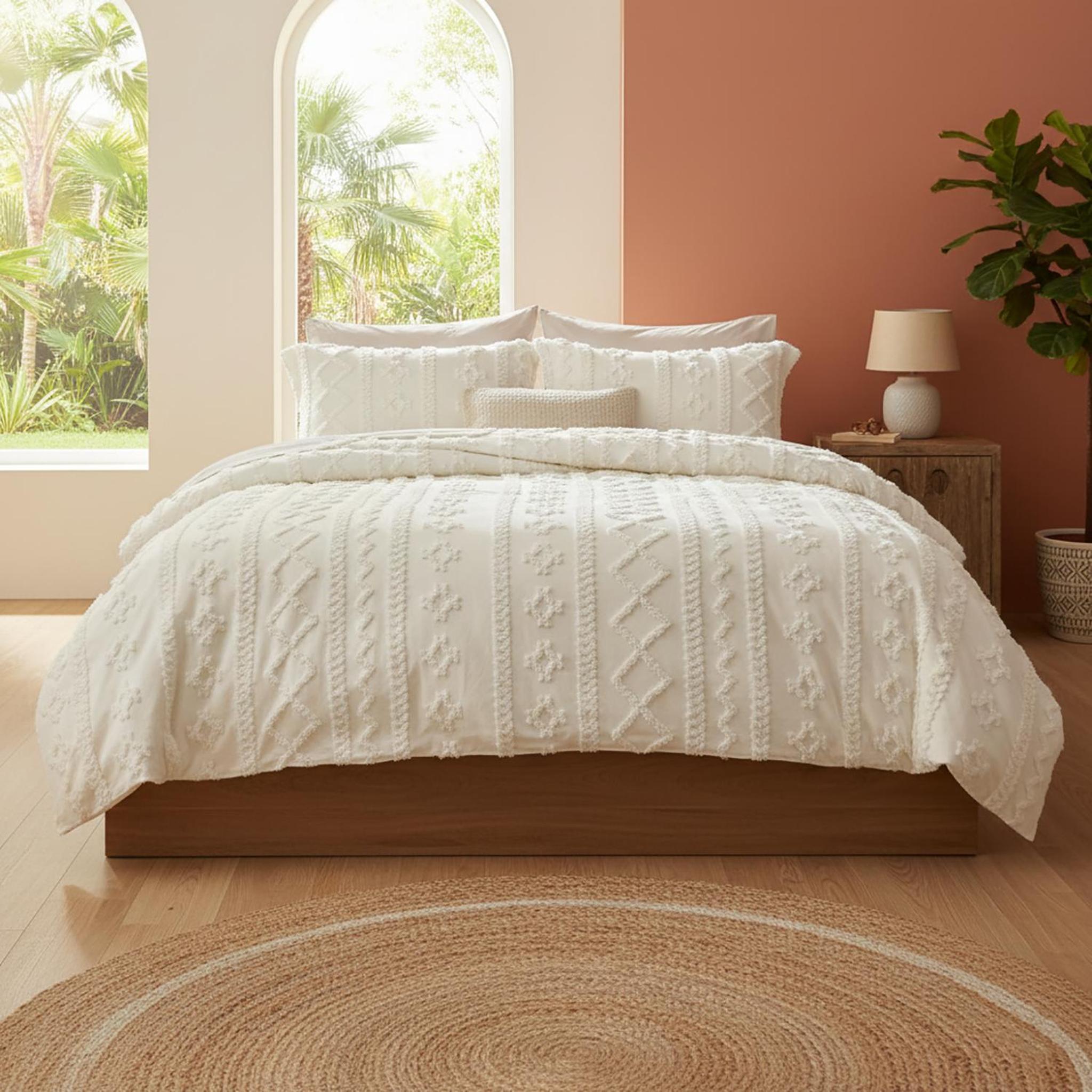 White tufted boho queen comforter set on a wooden bed, with decorative pillows and a natural fiber rug.
