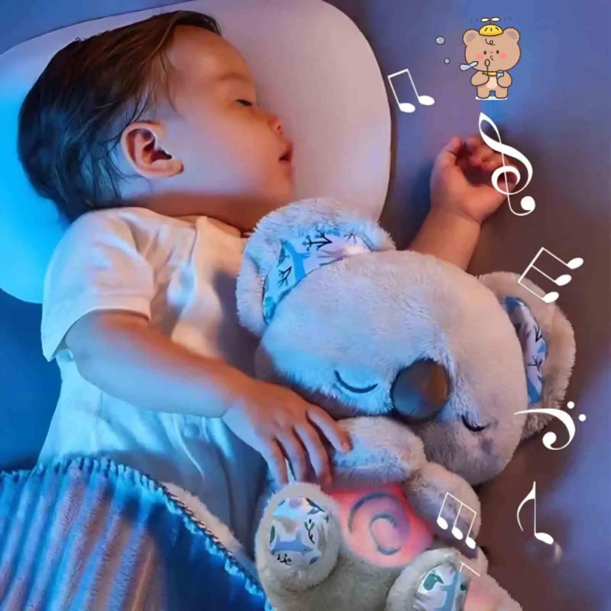Sleeping baby cuddling a grey plush koala toy with a glowing pink belly and music notes.