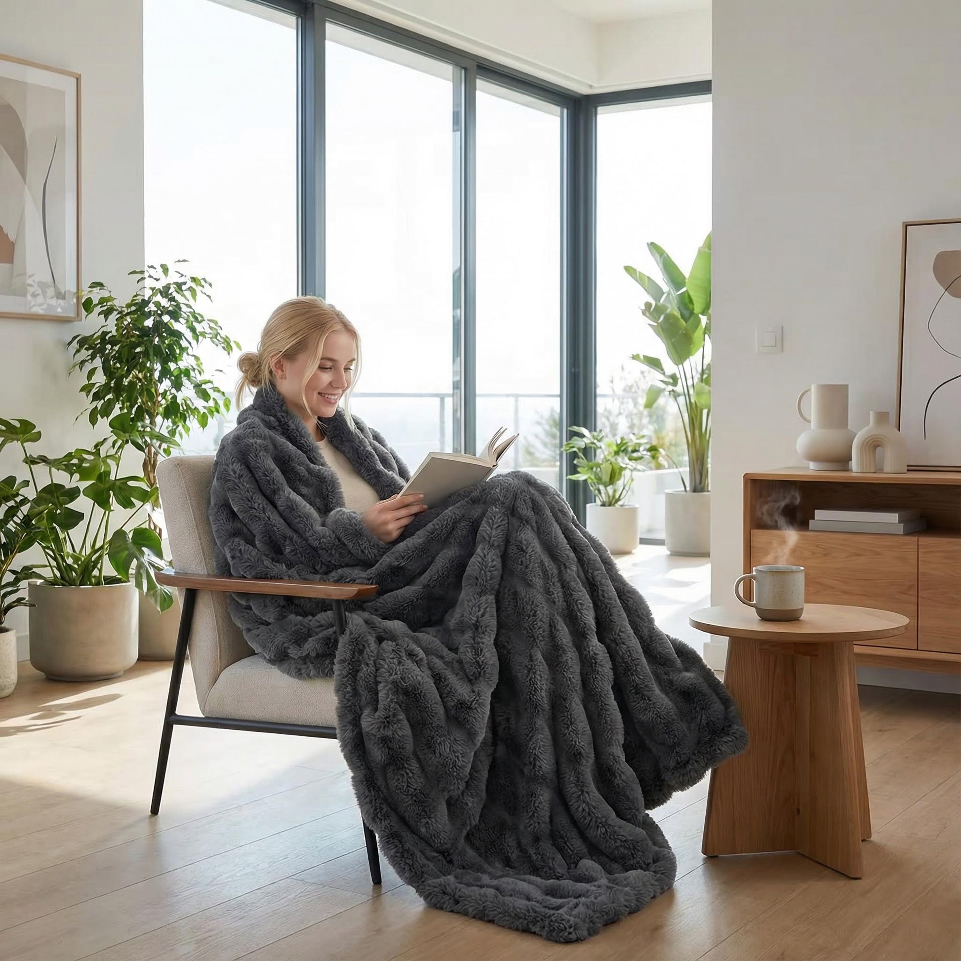 Woman relaxing in a chair, wrapped in a cozy dark gray bubble plush throw blanket, reading a book.