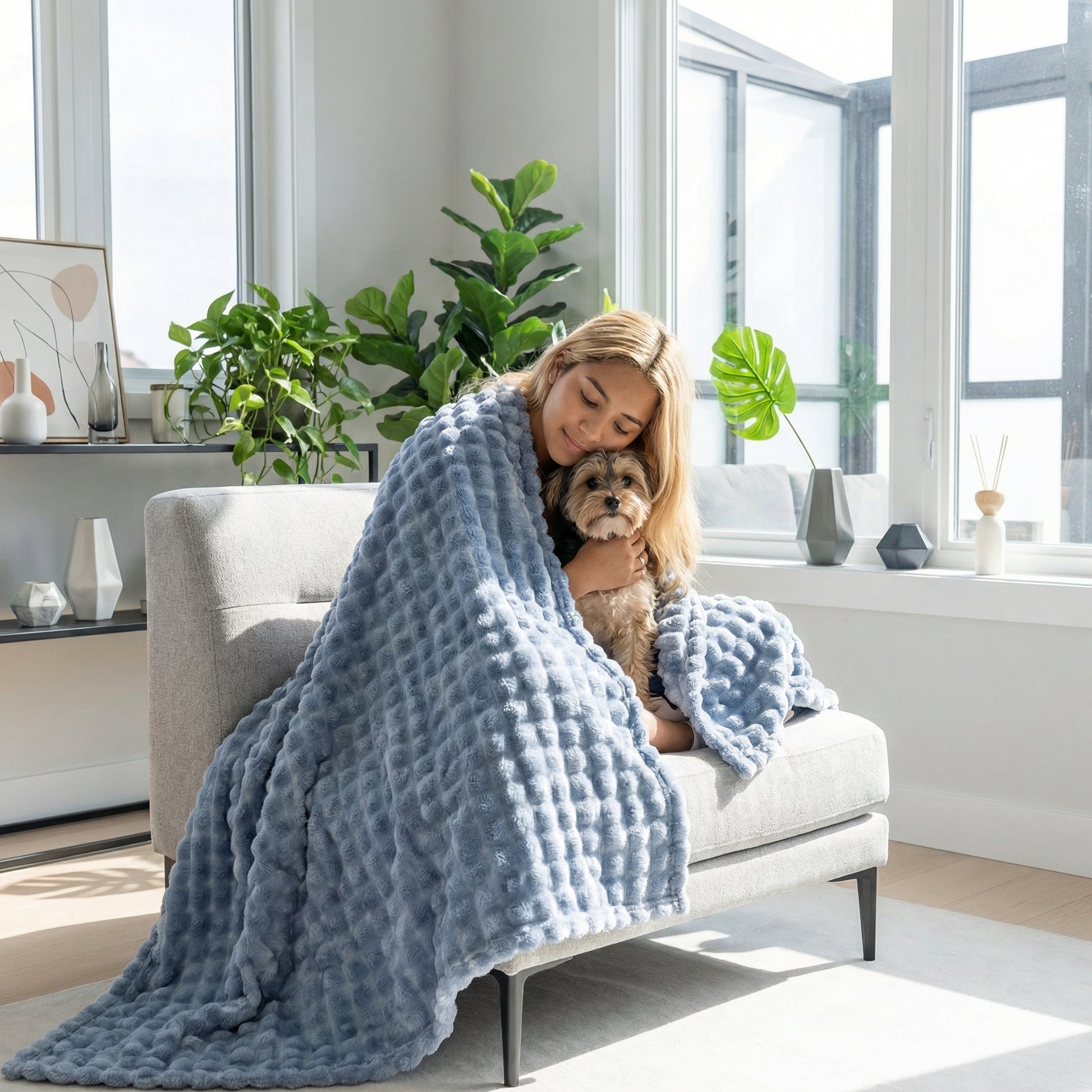 Woman and small dog snuggled in a soft, light blue Bubble Rabbit Flannel Blanket on a modern sofa.