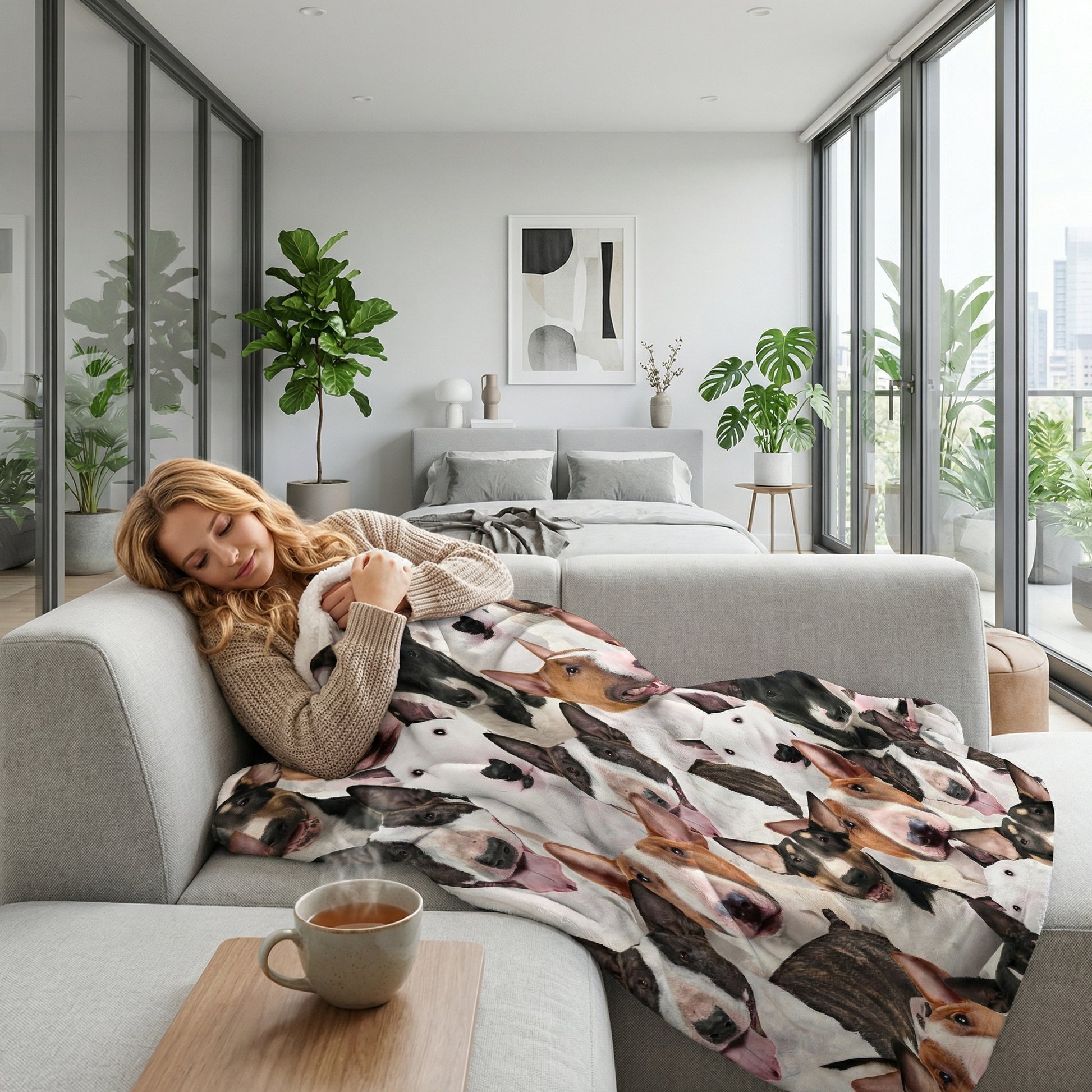 Blonde woman napping on a gray couch, covered by a soft Sherpa blanket with a 3D print of Bull Terrier dogs.