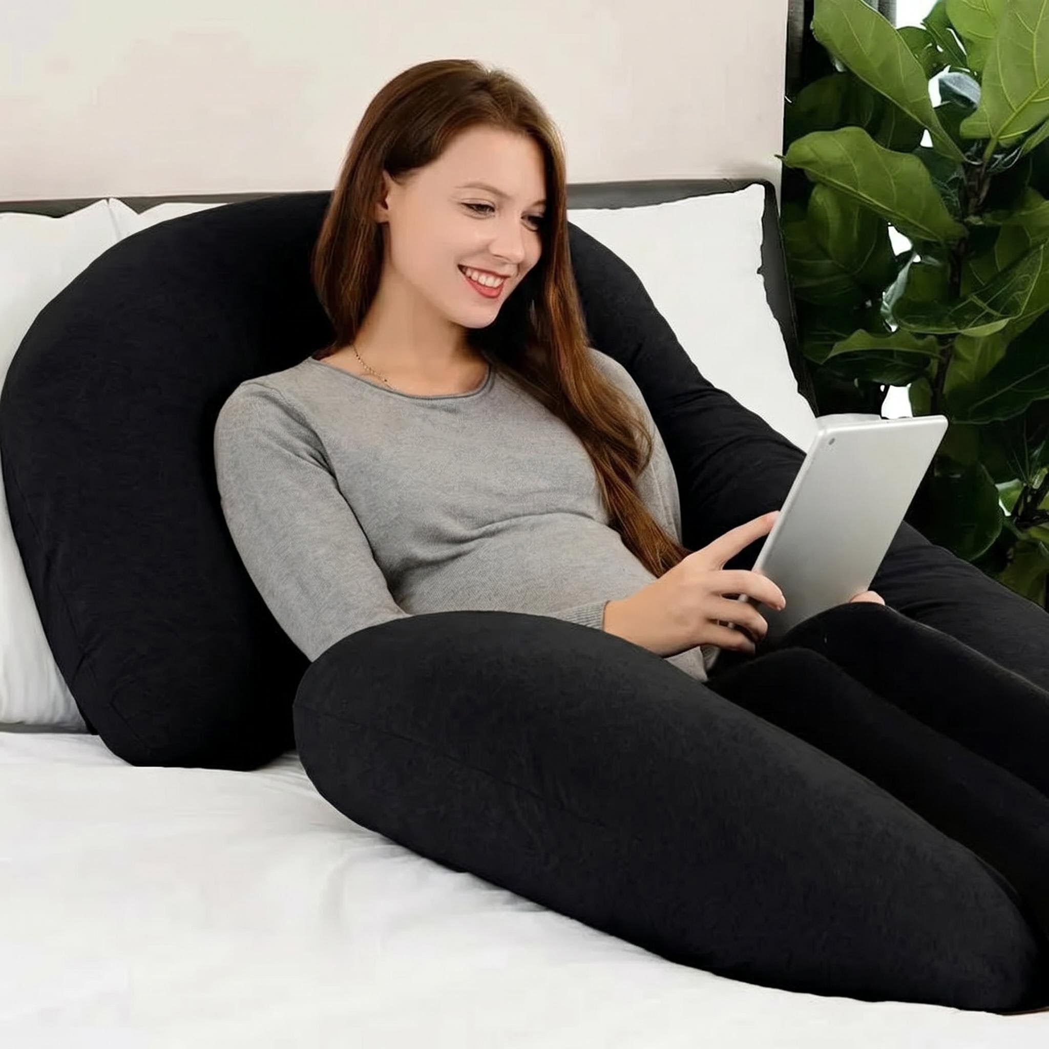 Smiling woman relaxing with a black C-shaped support pillow and tablet in bed.