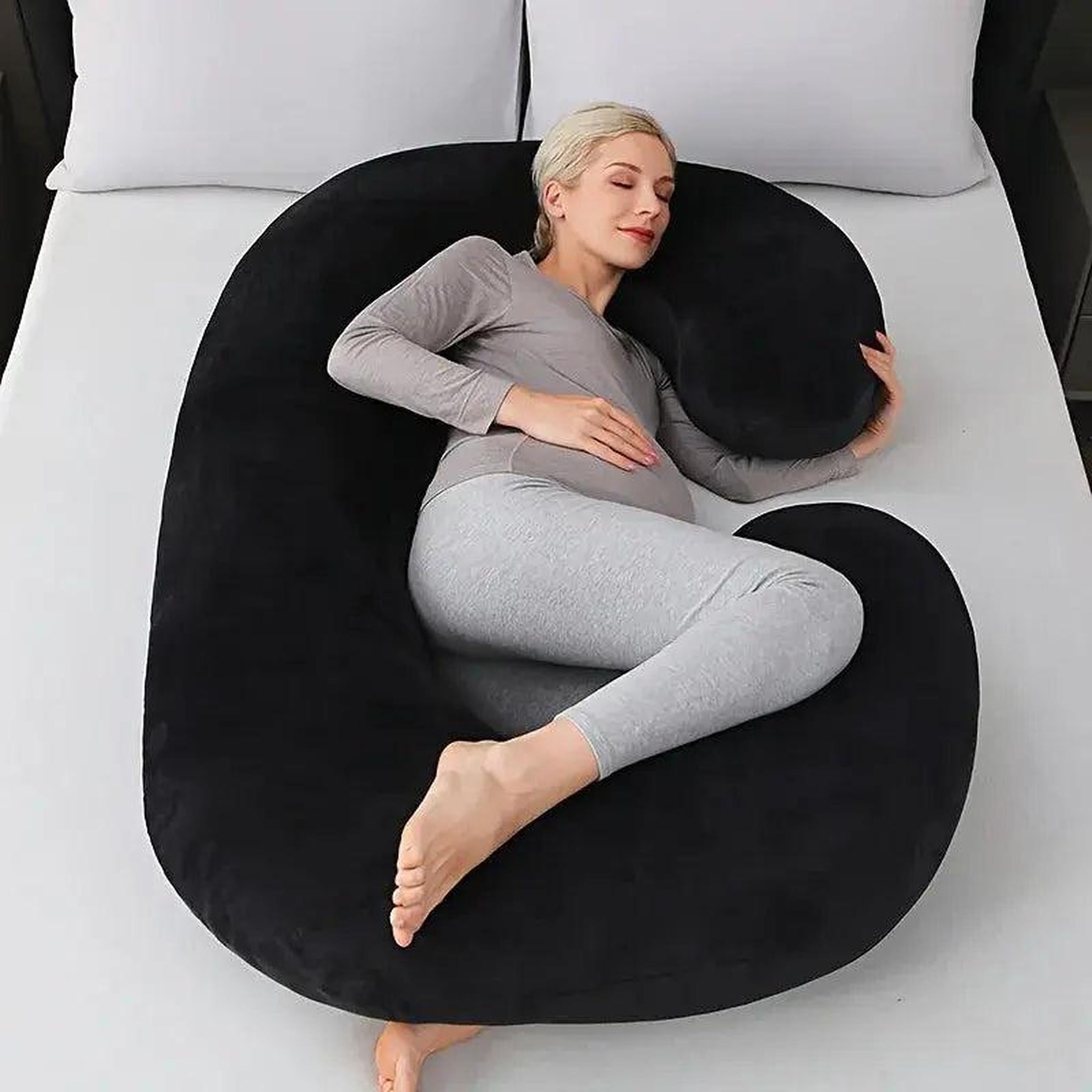 Pregnant woman resting on a large black C-shaped support pillow on a bed.