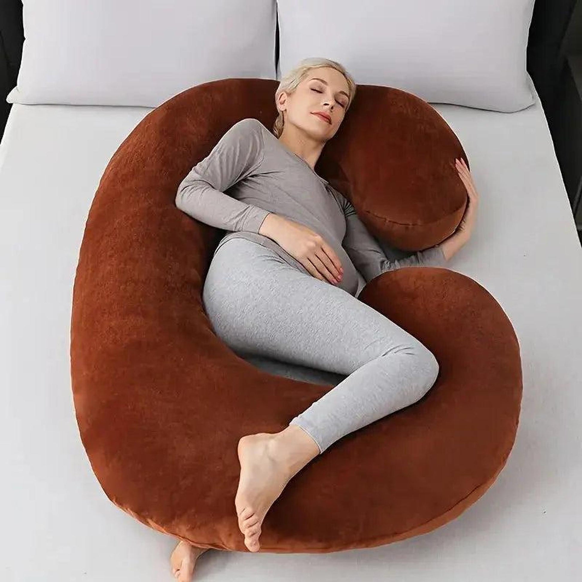 Woman side resting on a large brown C-shaped support pillow on a bed.