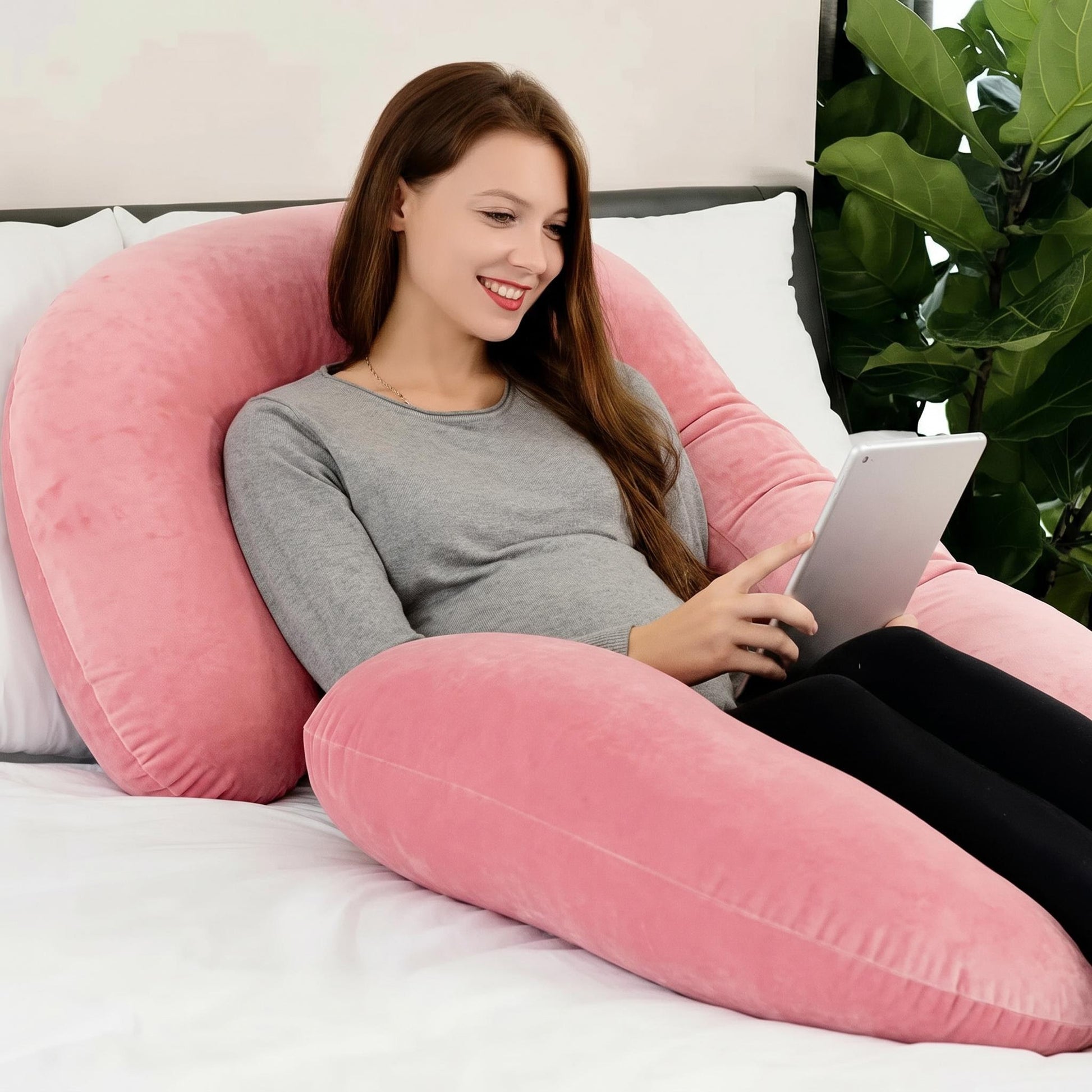 Woman resting comfortably on a large, pink C-shaped support pillow, using a tablet.