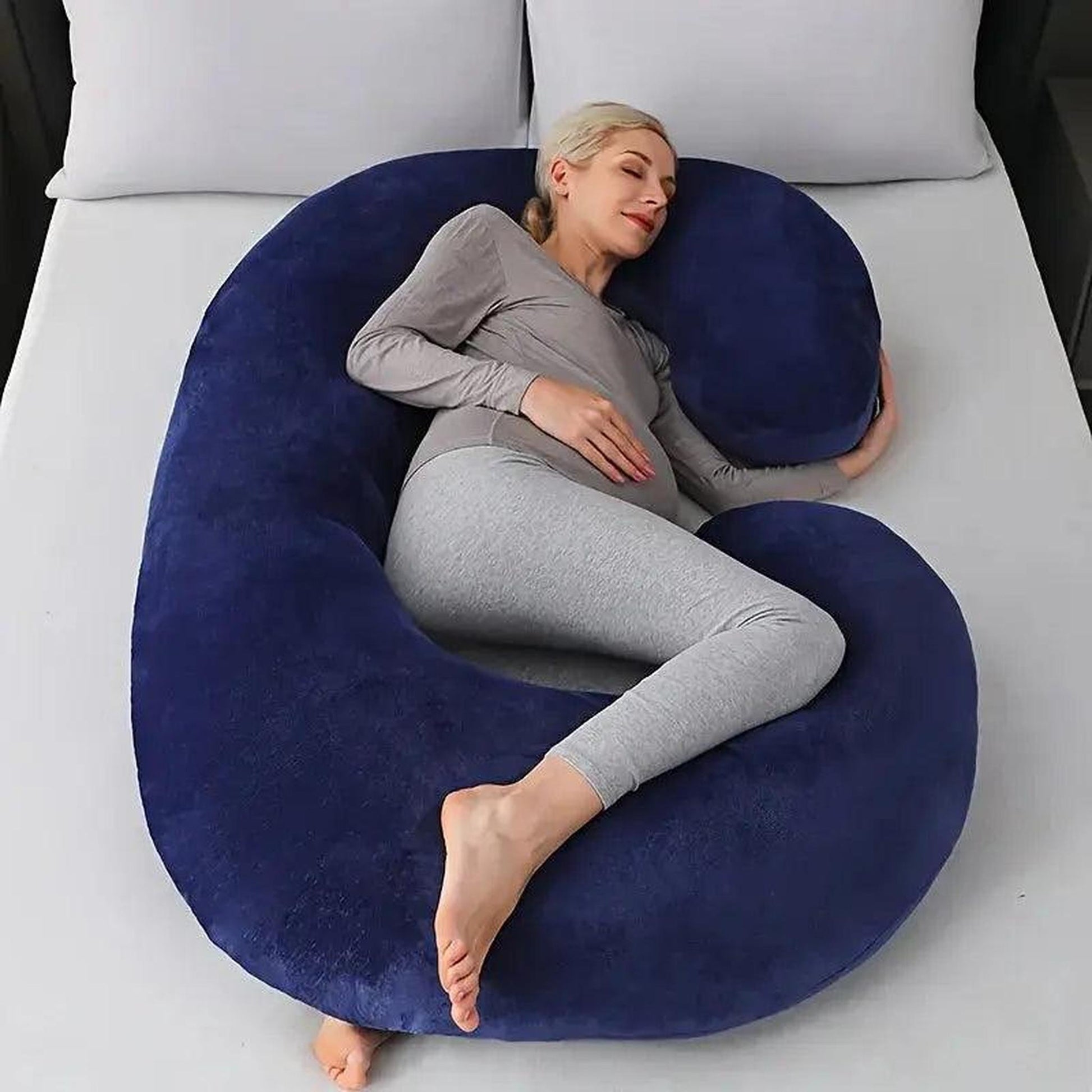 Pregnant woman sleeping peacefully on a large, plush navy blue C-shaped support pillow.