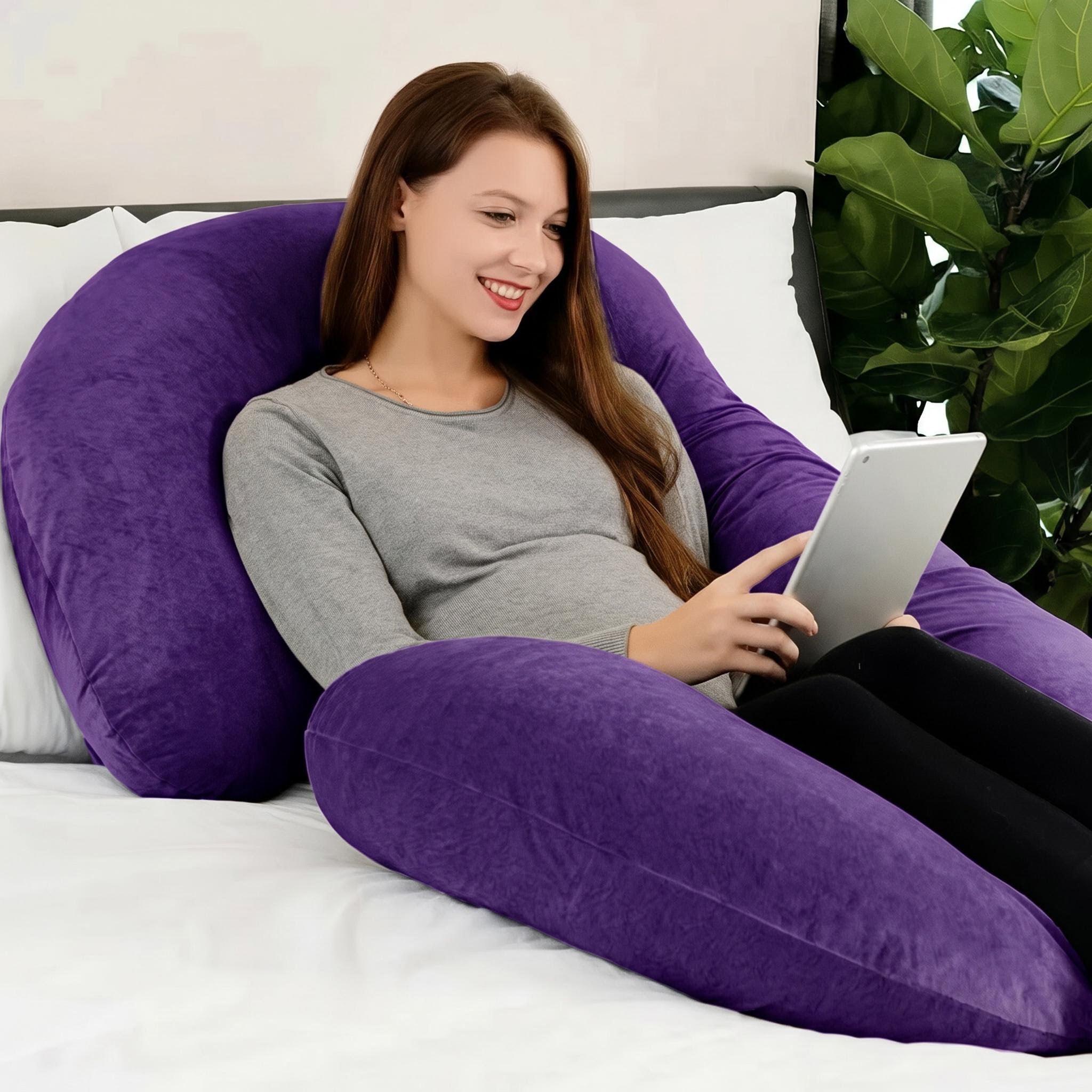 Smiling woman relaxing on a large purple C-shaped support pillow, holding a tablet.