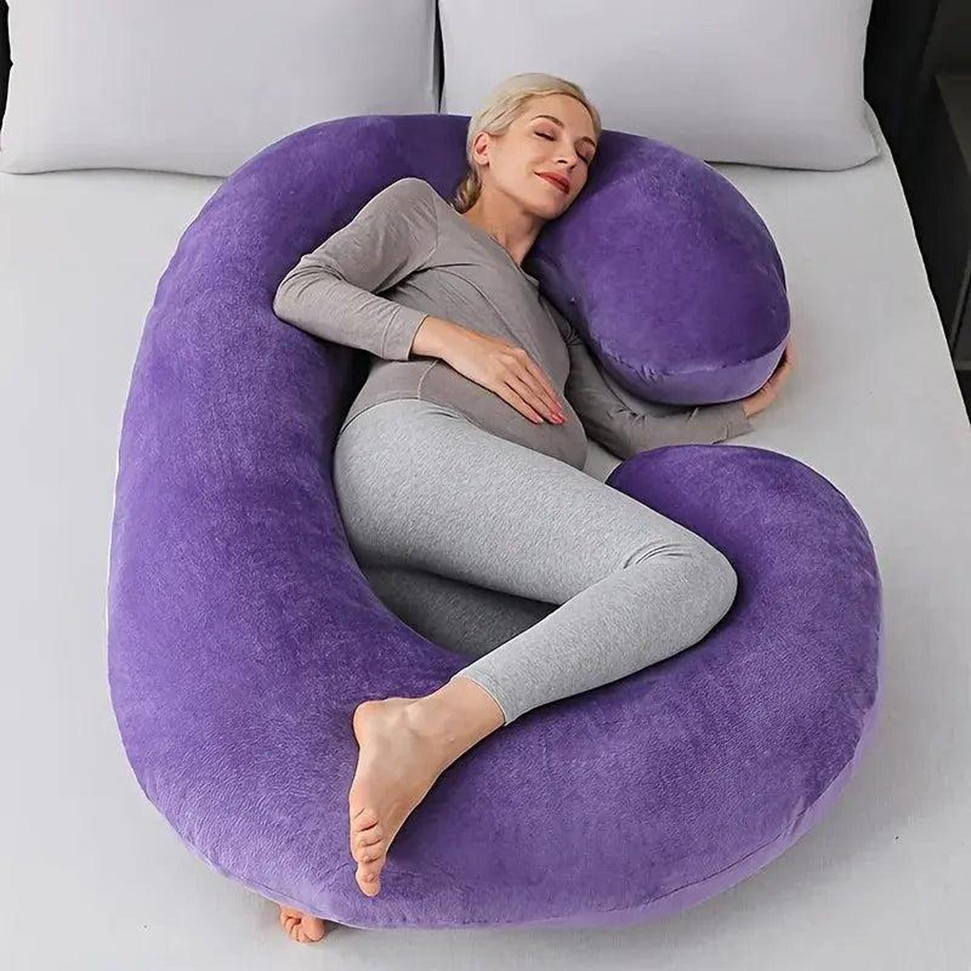 Pregnant woman sleeping comfortably on a large purple C-shaped support pillow.