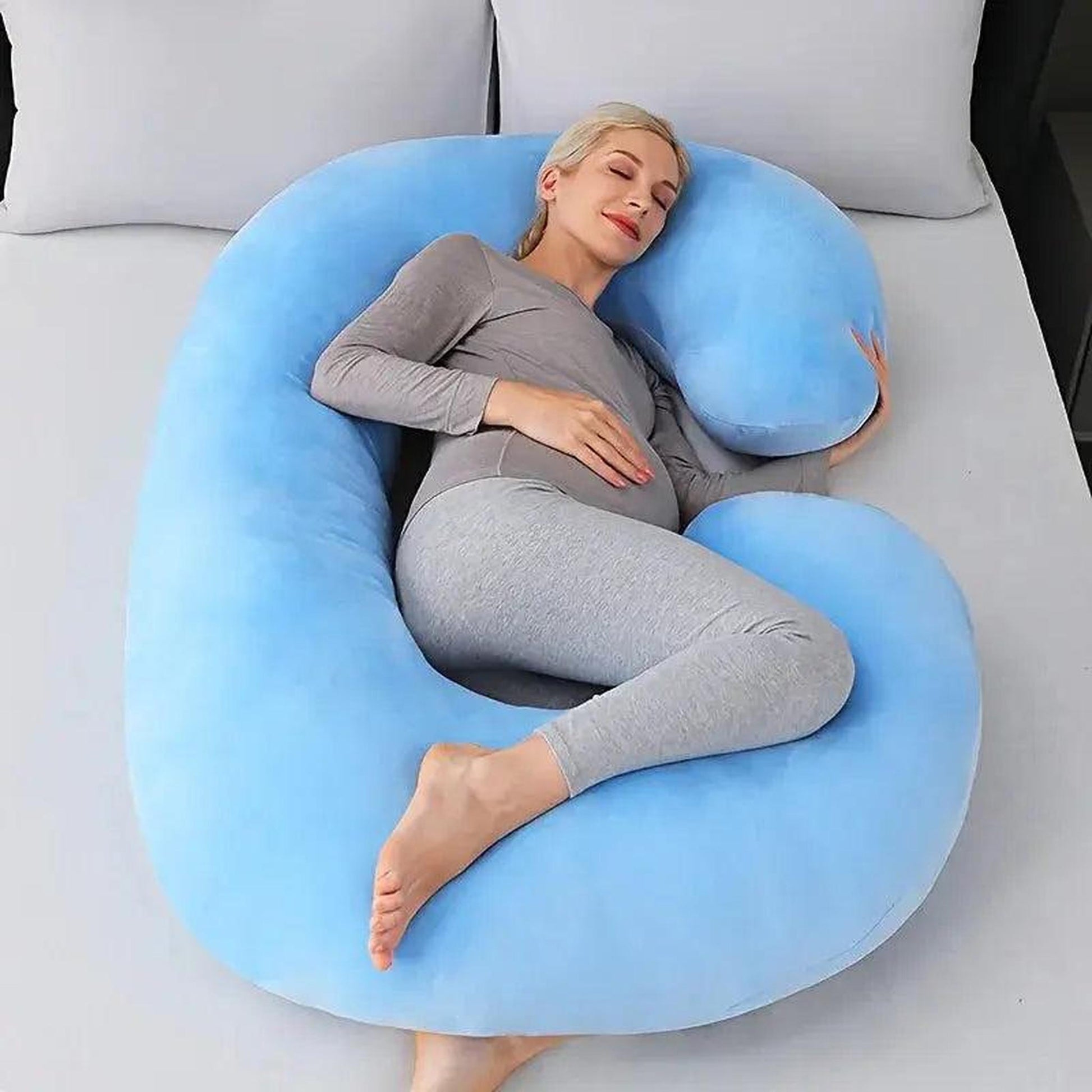 Pregnant woman resting comfortably on a large, light blue C-shaped support pillow.