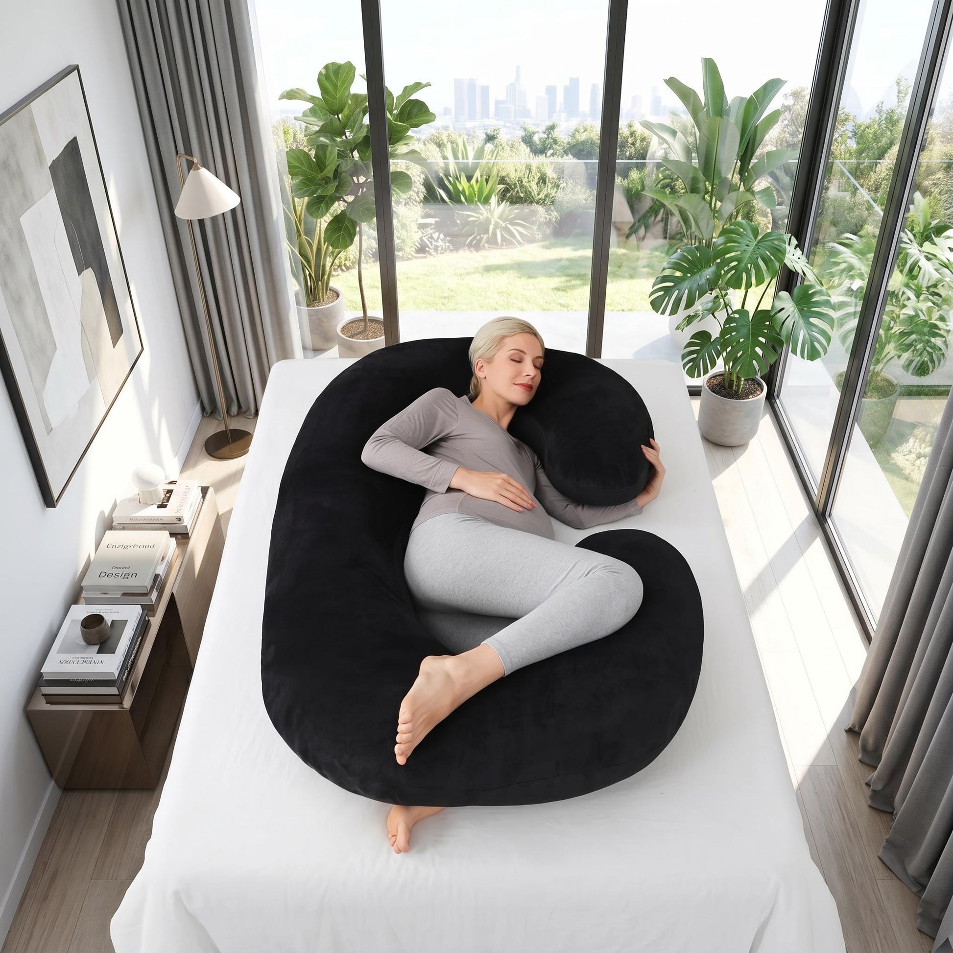 Woman resting on a large black C-shaped support pillow on a bed, ideal for side sleeping.
