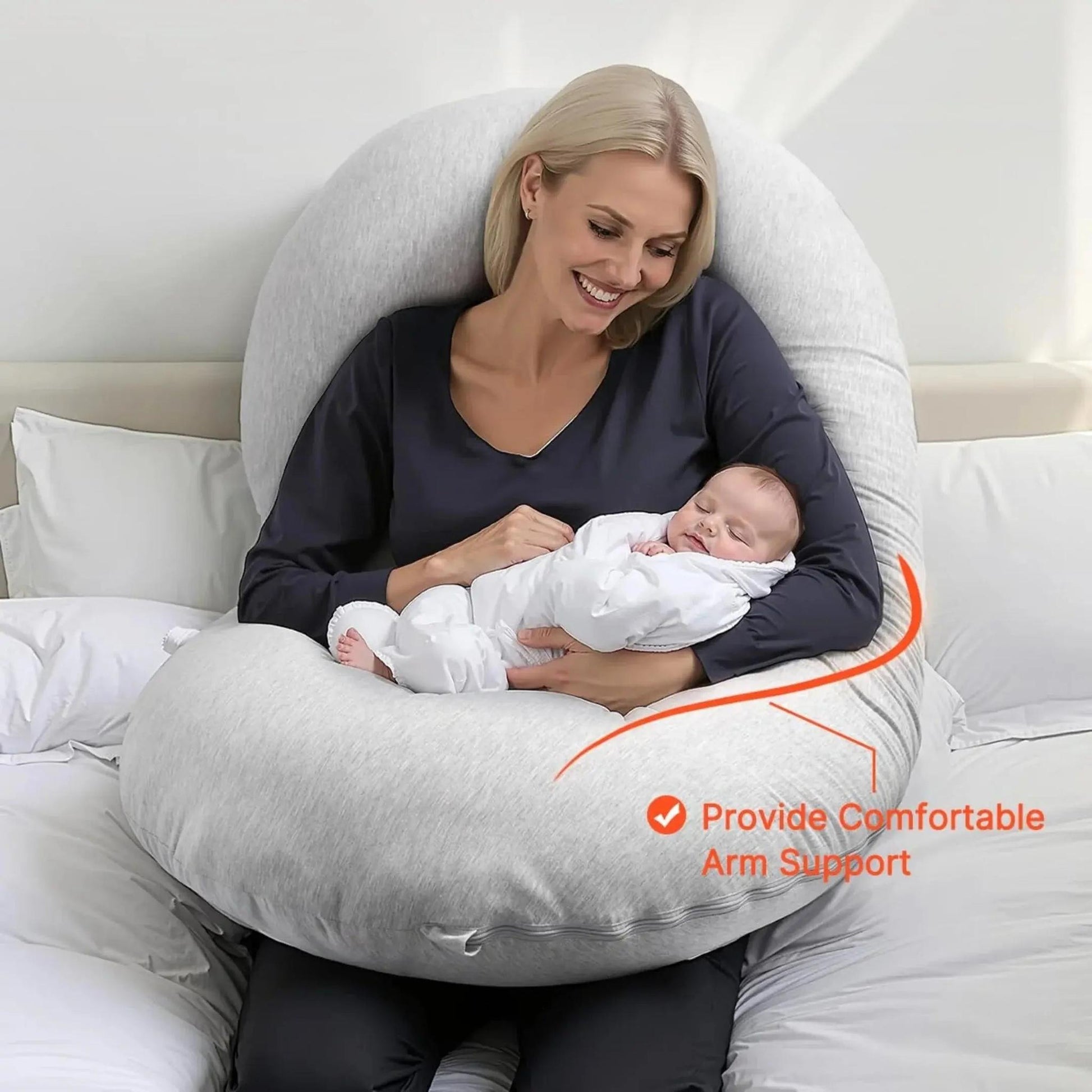 Smiling woman holding a sleeping baby, embraced by a light gray C-shaped support pillow.