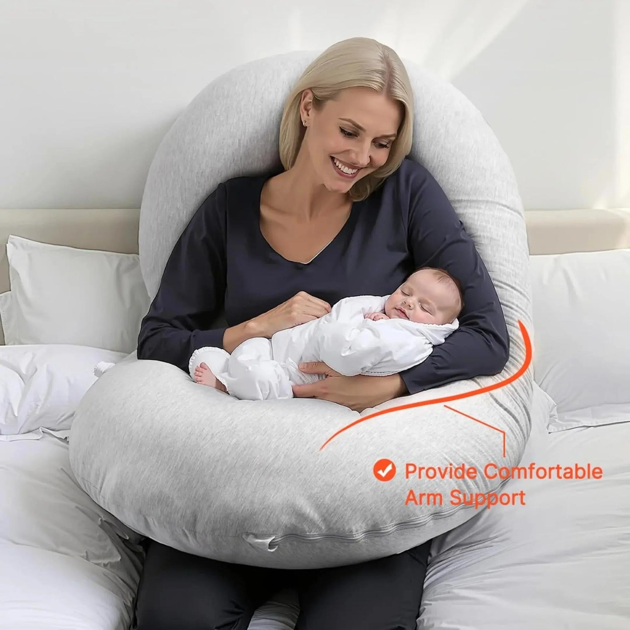 Smiling woman holding a sleeping baby, embraced by a light gray C-shaped support pillow.